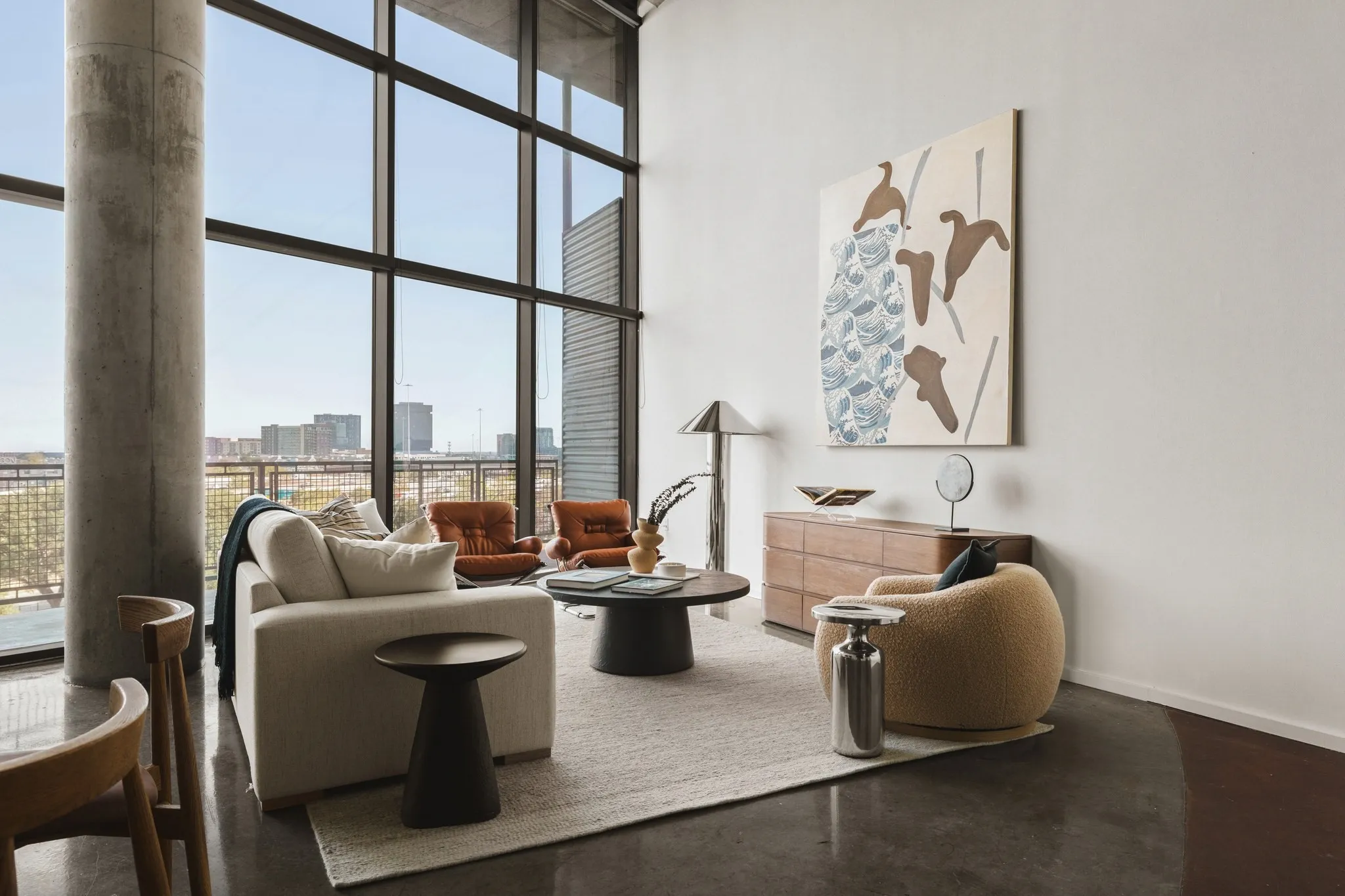 Expansive floor-to-ceiling windows, exposed concrete column, polished concrete flooring, white walls, and a light-toned area rug