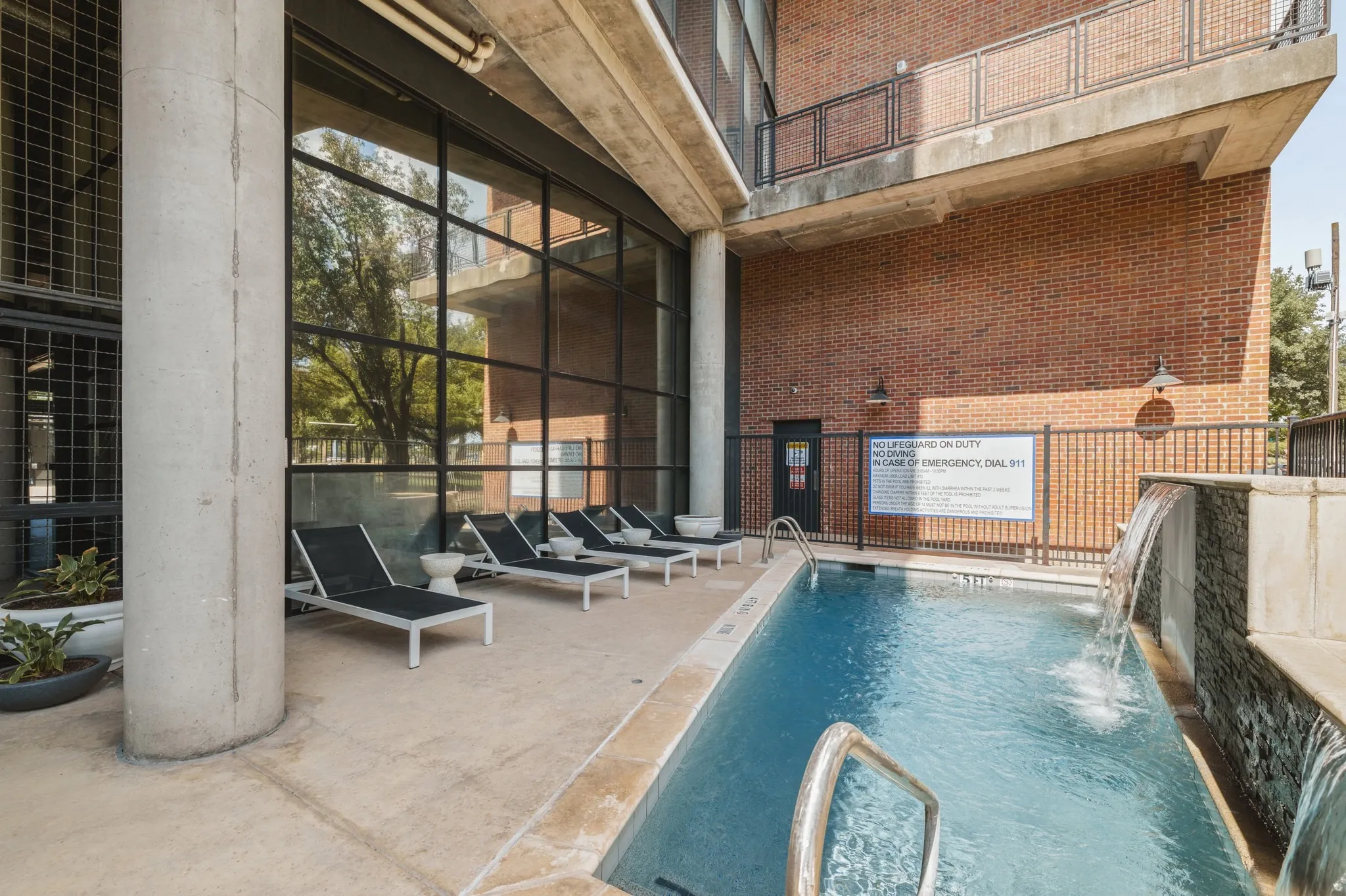 Outdoor swimming pool with water features, surrounding lounge area, and full-height windows