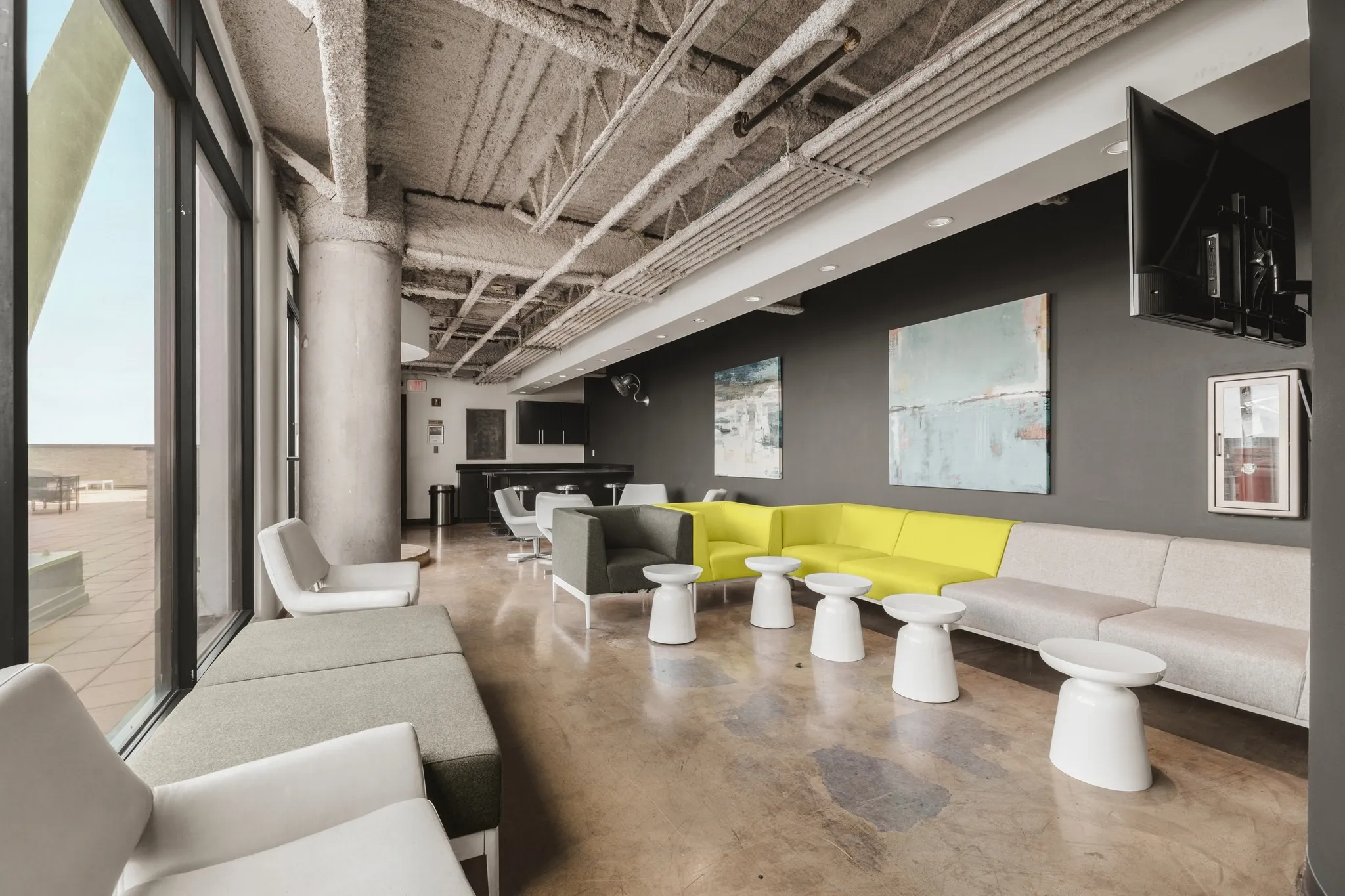 Expansive window line, exposed structural ceiling, polished concrete flooring, built-in bar area, and recessed lighting