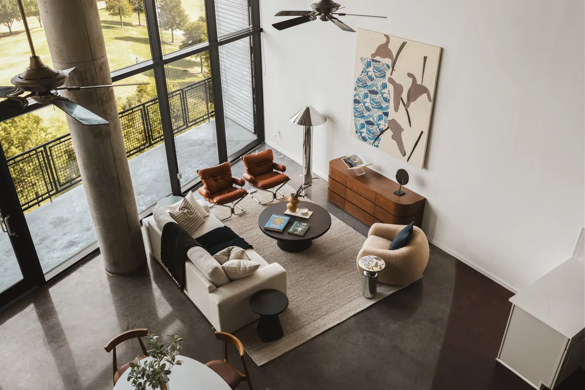Expansive floor-to-ceiling windows, polished concrete flooring, a private balcony with metal railings, a modern ceiling fan, and a built-in wall unit