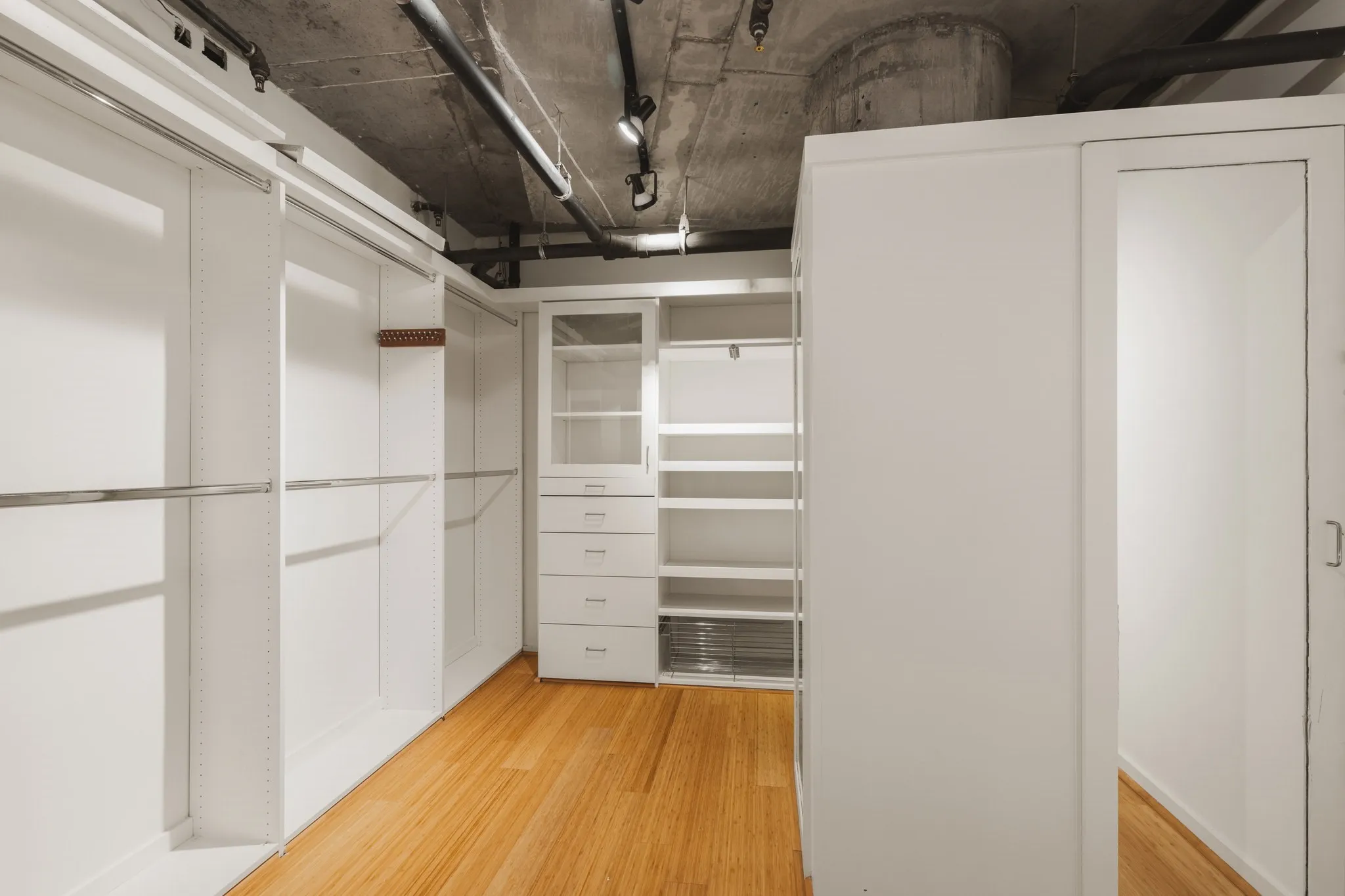 Built-in white cabinetry, exposed concrete ceiling, track lighting, and wood-finish flooring