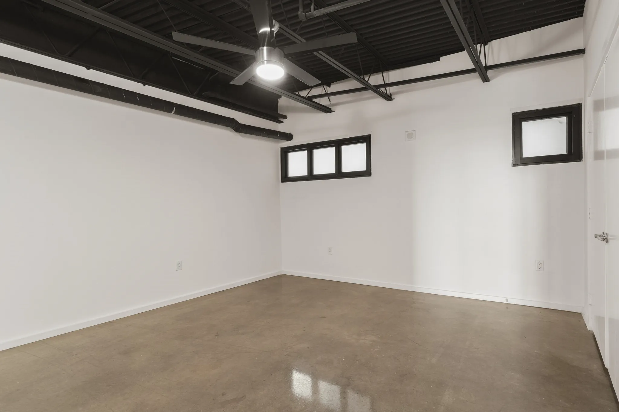 Exposed black ceiling joists, concrete flooring, and multiple high windows