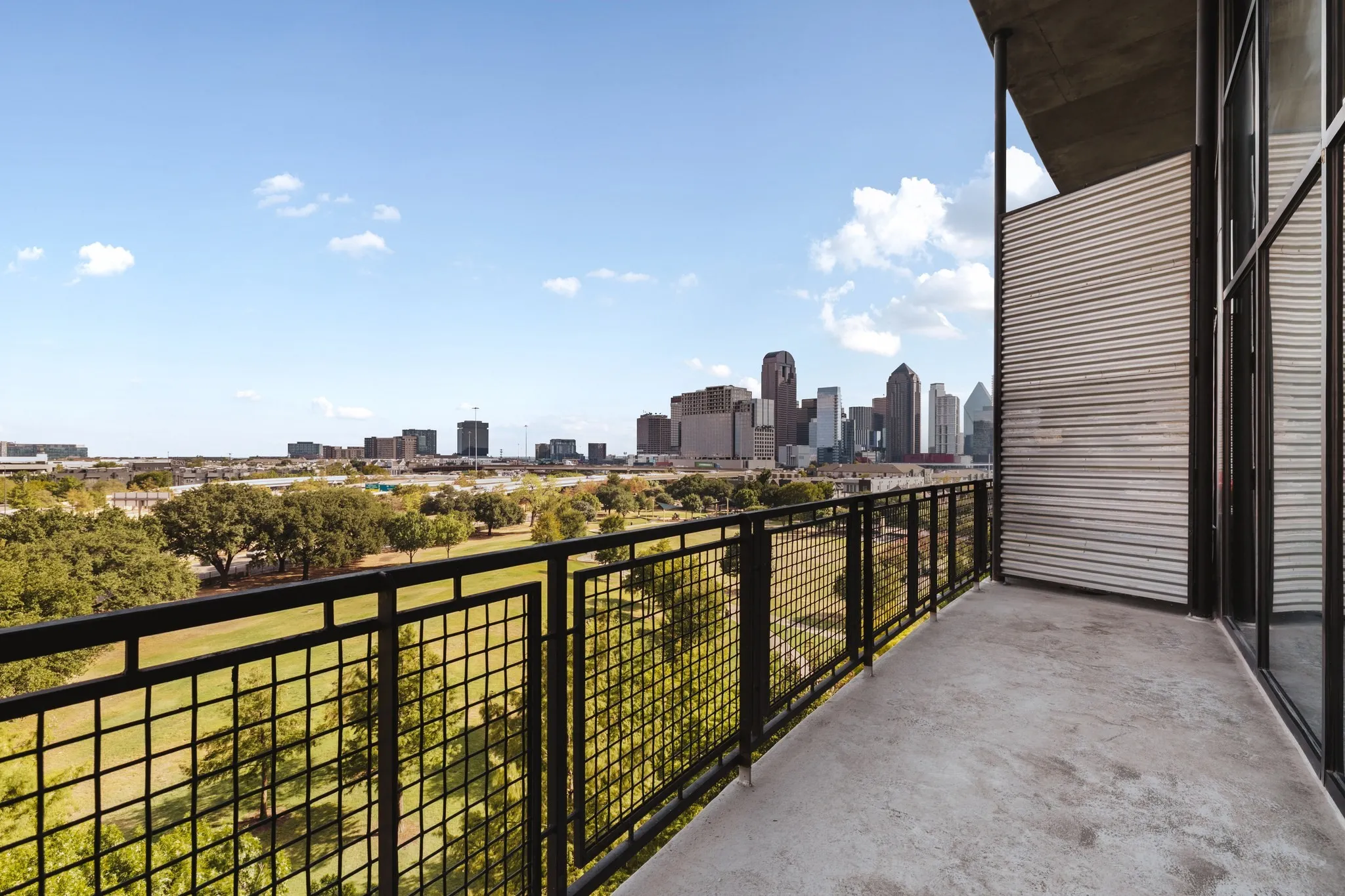 Concrete balcony with black metal railings, offering urban skyline and green space scenery