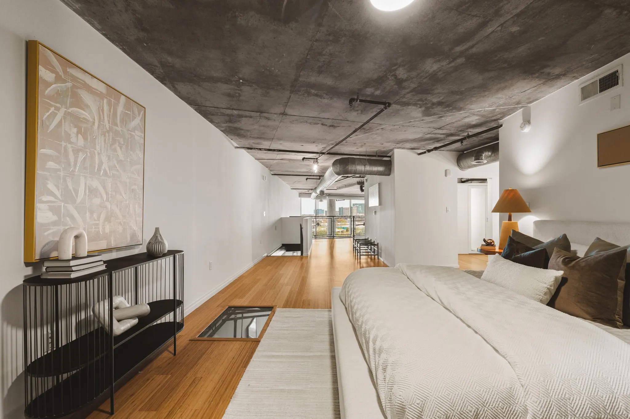 Exposed concrete ceiling with visible ductwork, wood-finish flooring, white walls, recessed lighting, and a glass floor panel