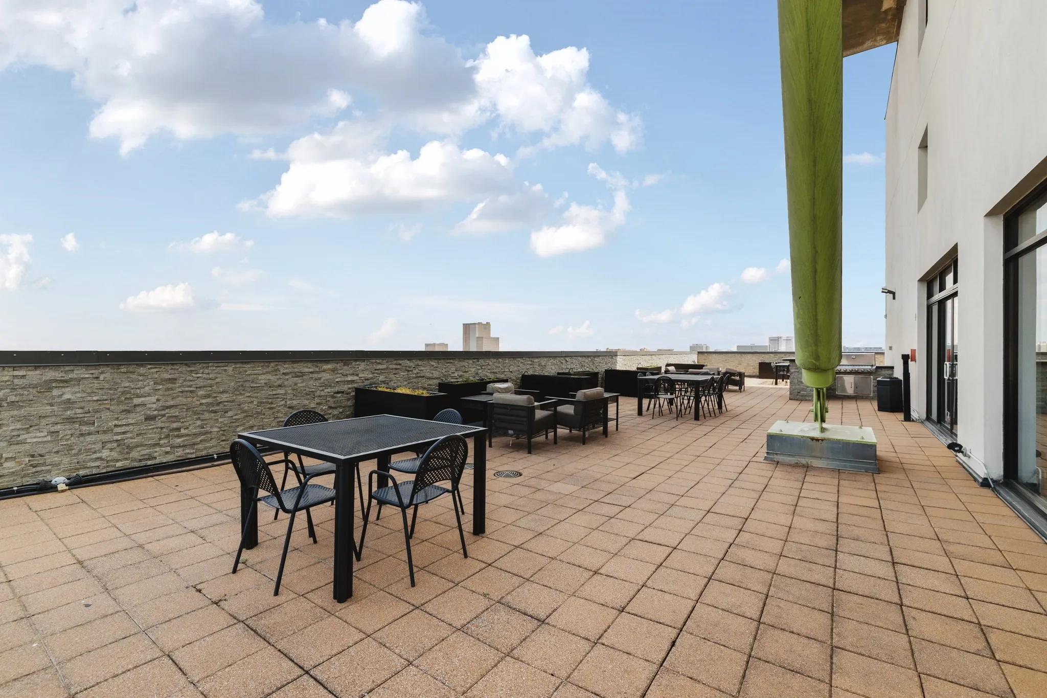 Expansive outdoor terrace featuring paver flooring, a perimeter wall, and a building exterior with large window openings