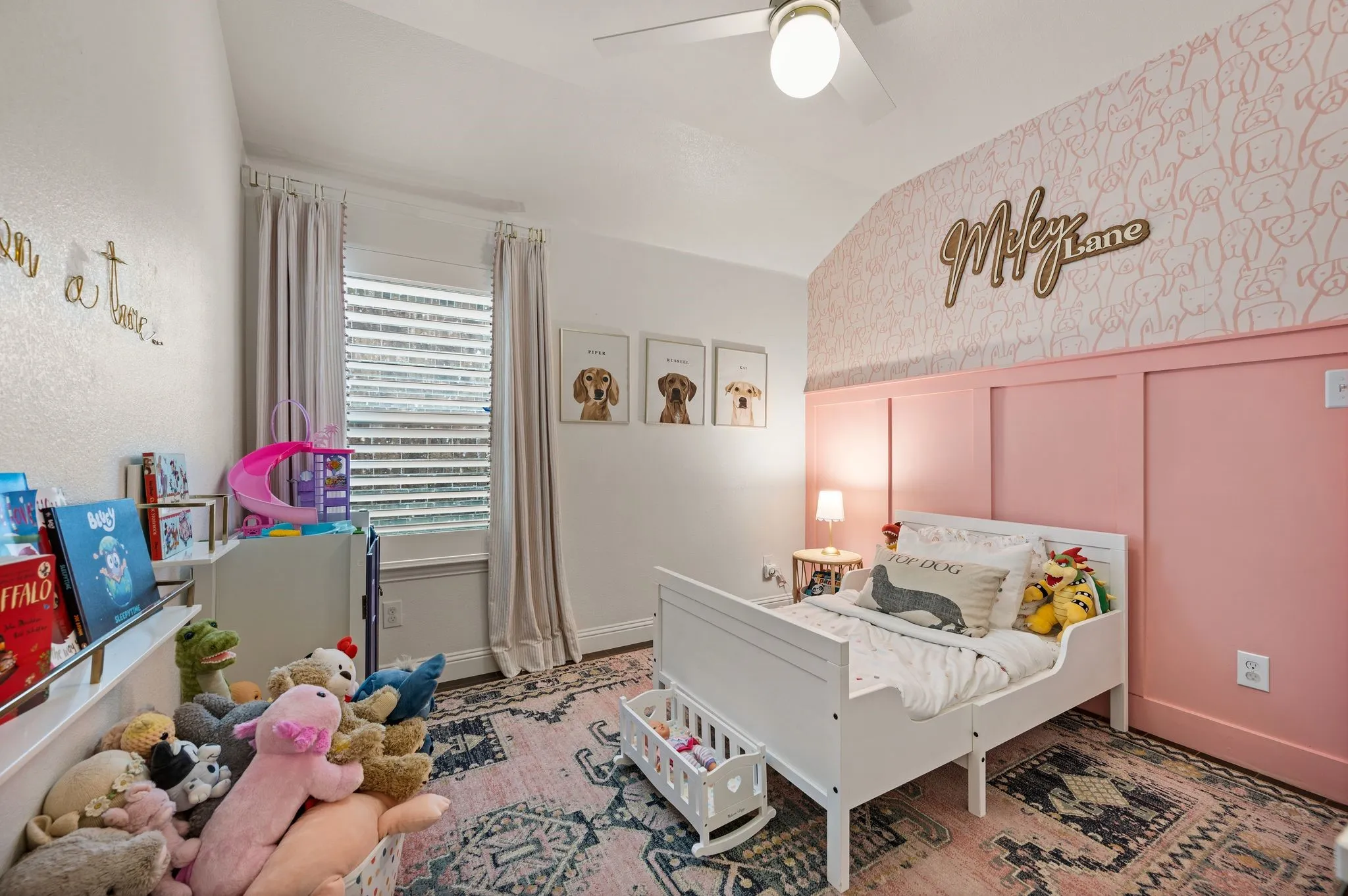 Guest bedroom with Accent wall with pink wainscoting and patterned wallpaper, with ceiling fan and window with upgraded shutters and flooring is the same wonderful flooring that is the same throughout the house!