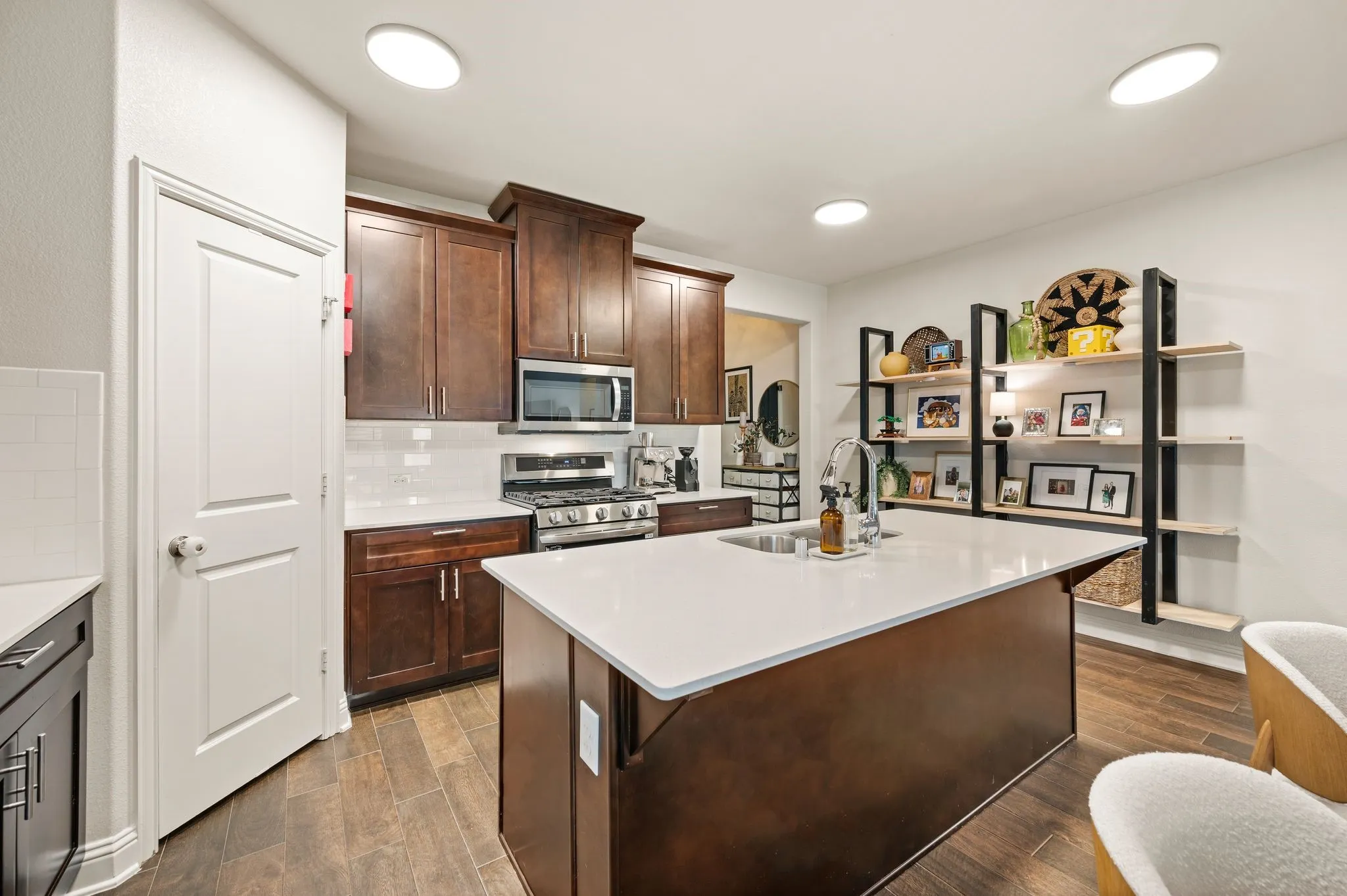 Kitchen featuring updated  flooring, dark wood cabinetry, white subway tile backsplash, quartz countertops and stainless steel appliances