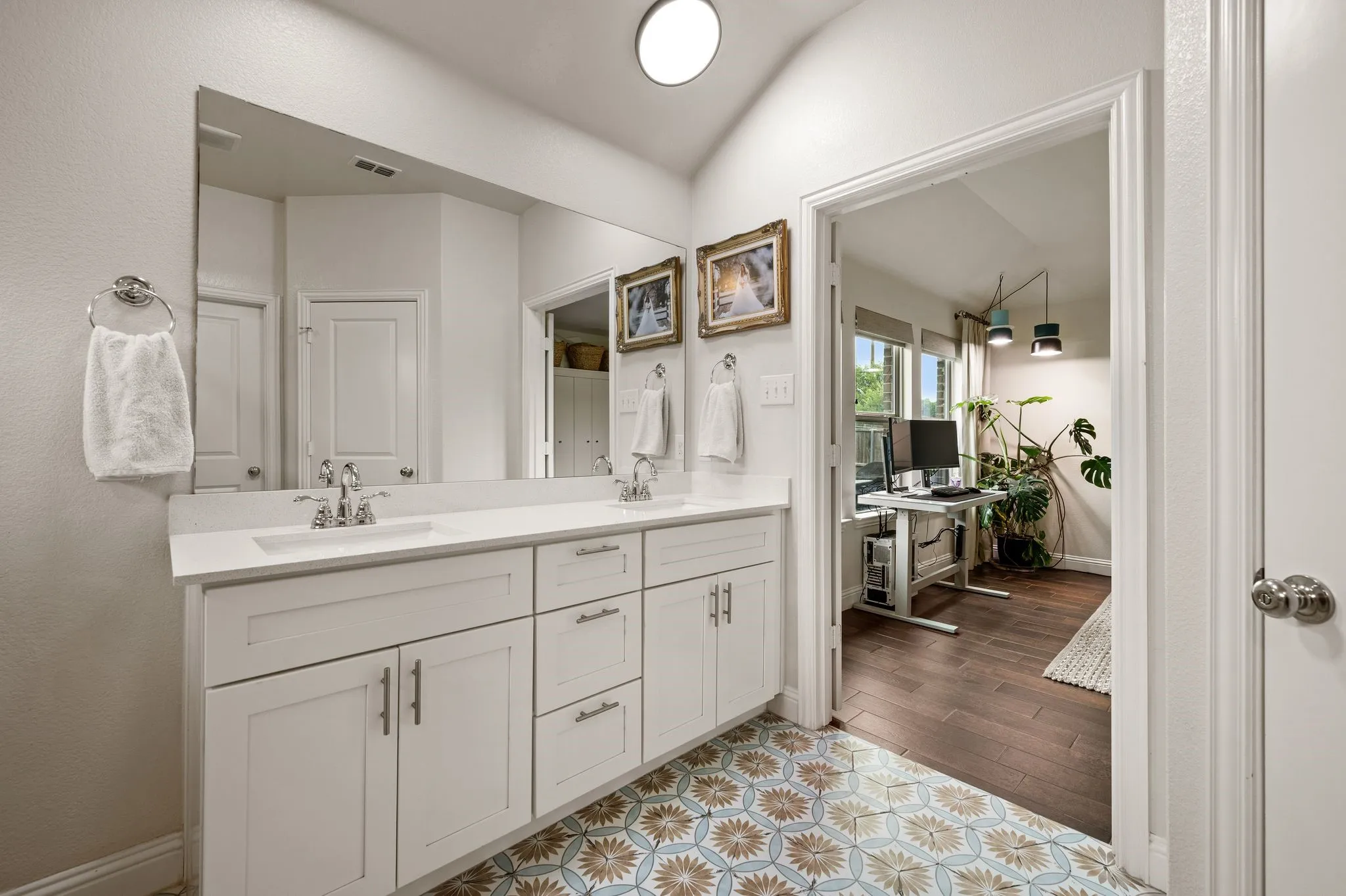 Primary bathroom has a Dual vanity with white cabinetry, and a quartz countertop, complemented by updated beautiful floor tiles and a vaulted ceiling...Perfect place to unwind and relax!