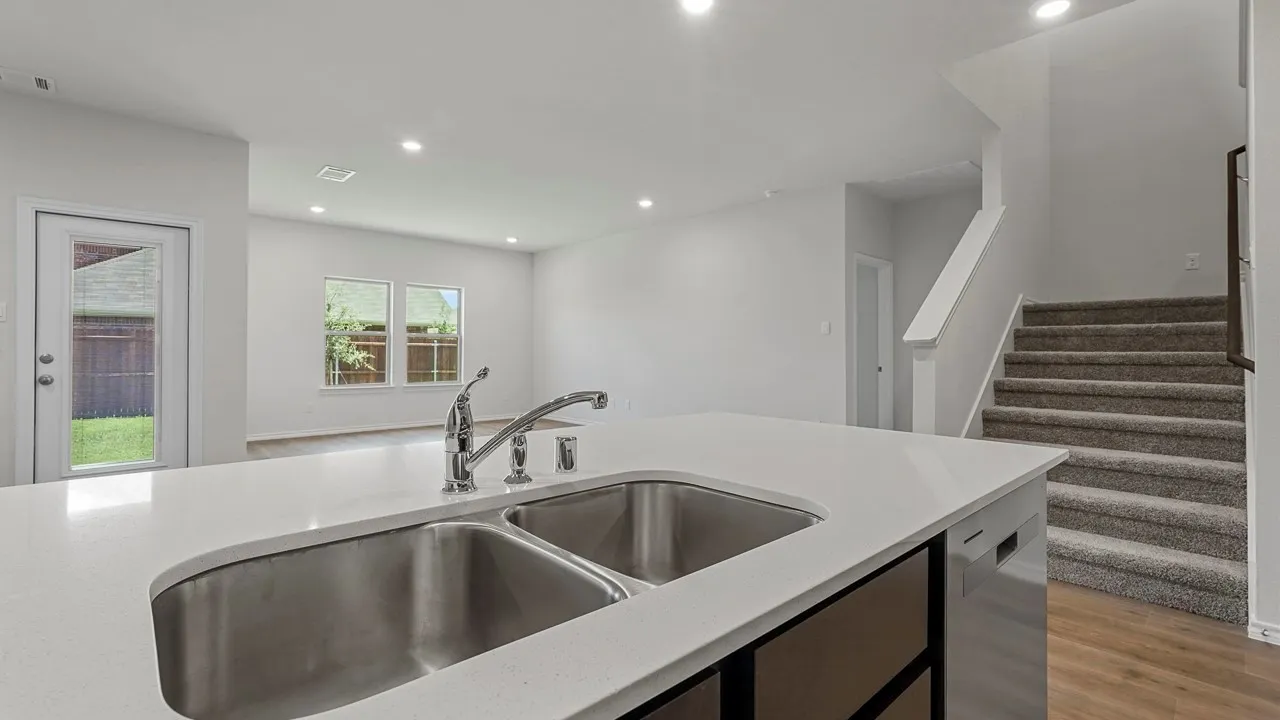 Kitchen island with dual stainless steel sink and chrome faucet, recessed lighting, wood-finish flooring, and carpeted staircase