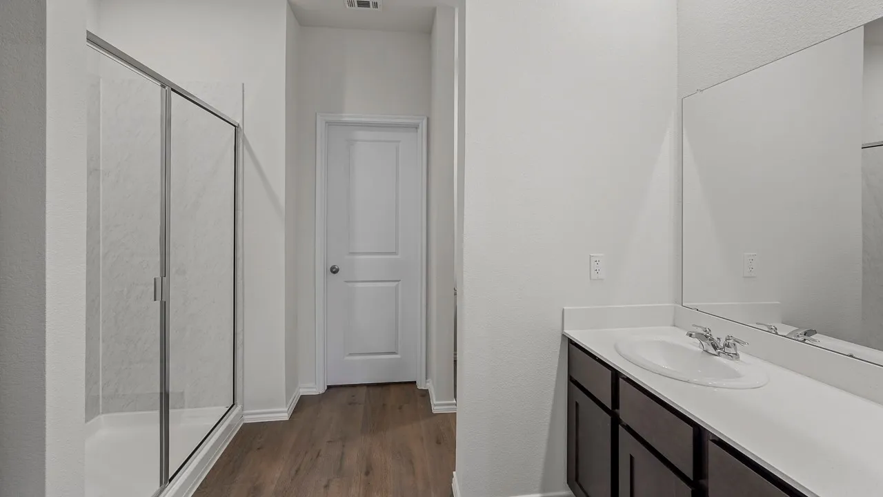 Wood-finish flooring, white vanity countertop, dark wood-finish cabinetry, and a walk-in shower with clear glass enclosure