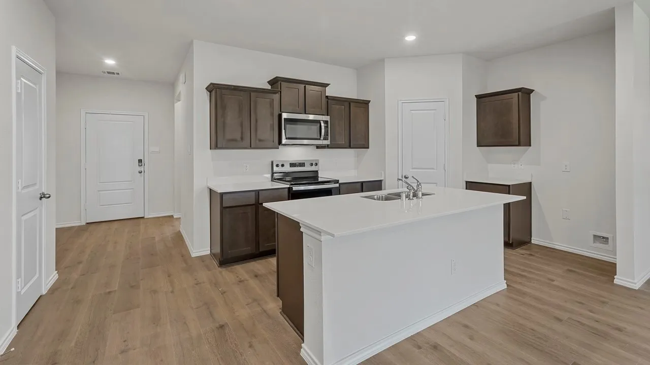 Kitchen featuring dark wood-finish cabinetry, stainless steel appliances, a center island with an integrated double sink, and light-toned countertops
