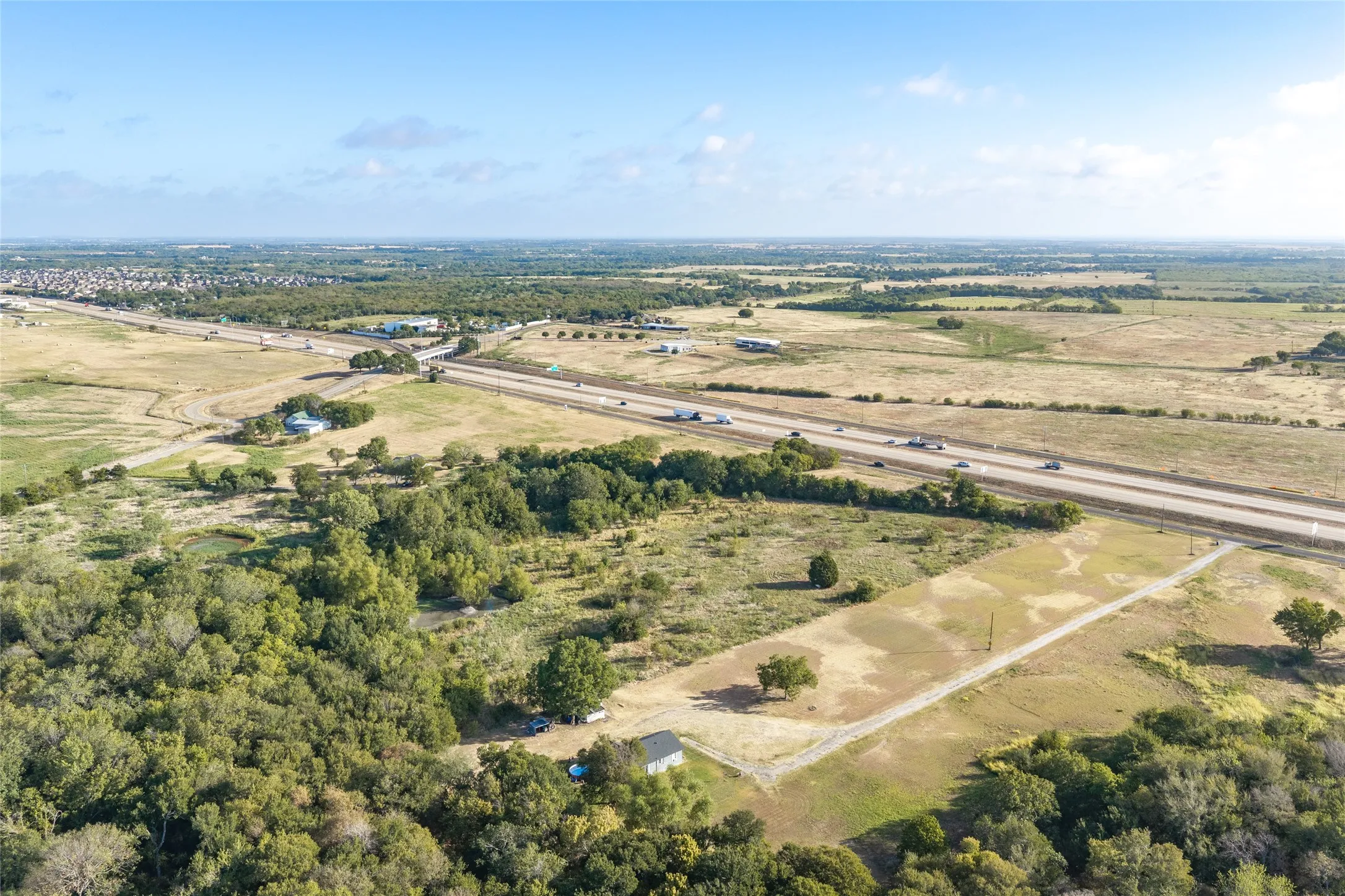 Expansive undeveloped land with a partial tree-line, a small pond, and proximity to a multi-lane highway
