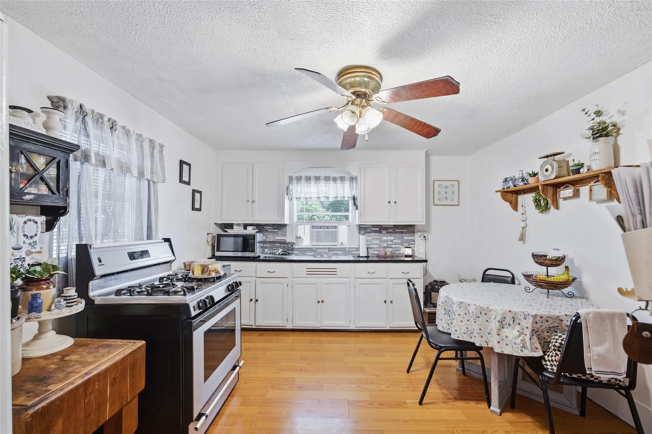 Hardwood flooring, white cabinetry, dark countertops, tile backsplash, and a ceiling fan with integrated lighting