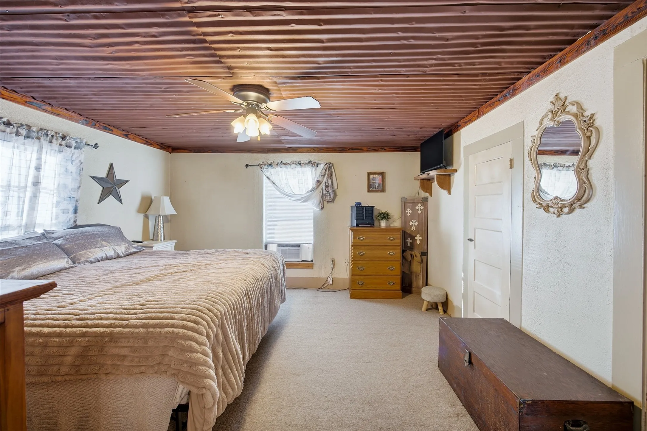Corrugated wood ceiling, ceiling fan with integrated lighting, wall-mounted shelving, paneled door, and carpeted flooring