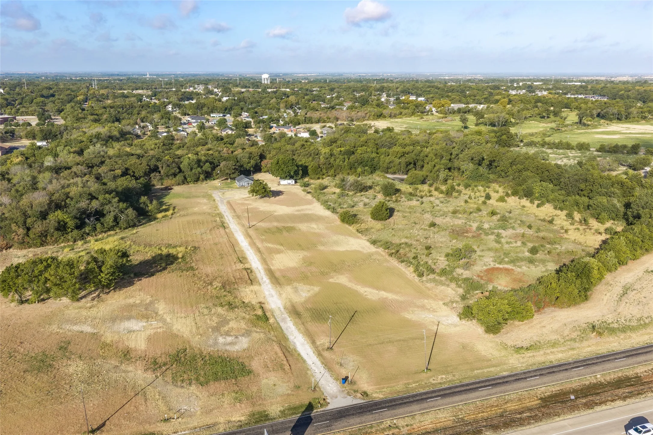 Expansive land parcel with a visible road frontage, established trees, and a distant water tower