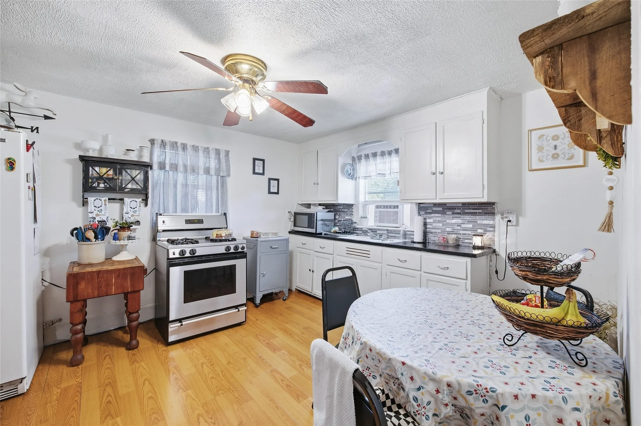 White cabinetry with dark countertops, stainless steel range, and wood-finish flooring