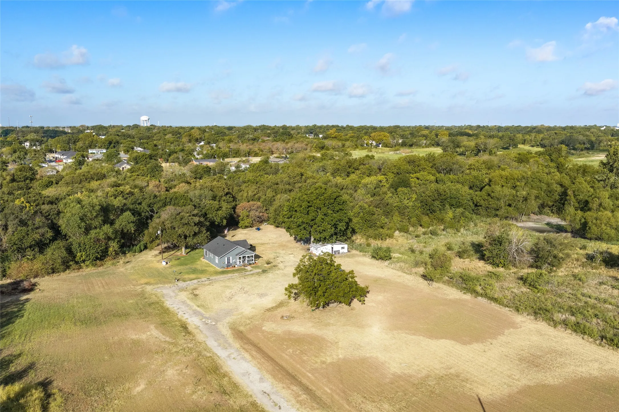 Expansive property featuring a detached dwelling with a dark shingle roof, a secondary structure, and a large natural area with scattered trees
