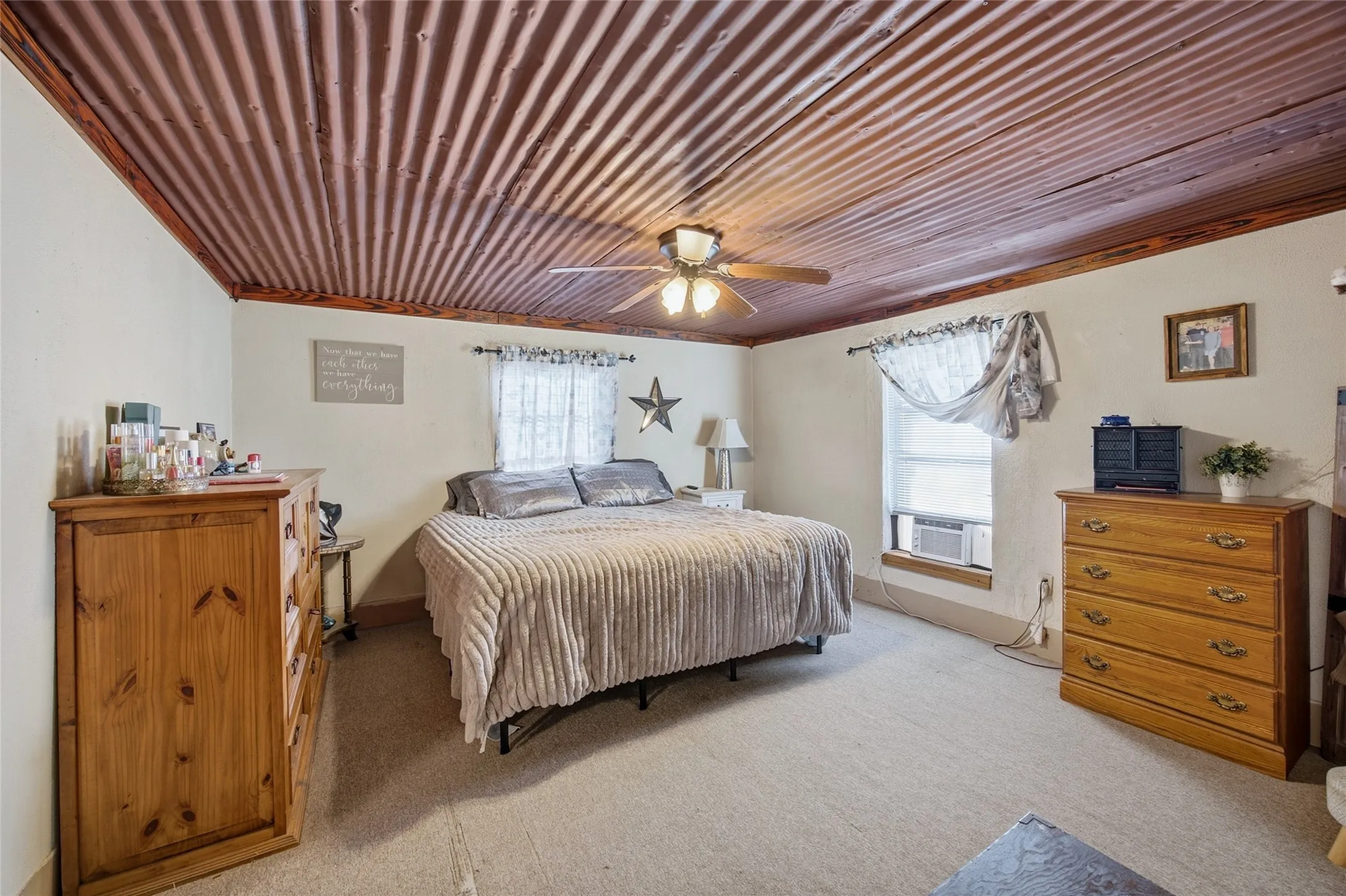 Corrugated wood-finish ceiling with exposed beams, ceiling fan with integrated lighting, two windows, and light-toned wall paint