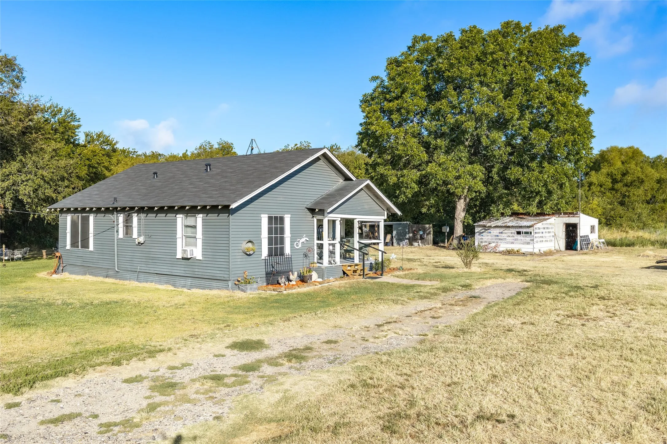 Exterior featuring gray siding, a dark shingle roof, white trim windows, and a covered porch