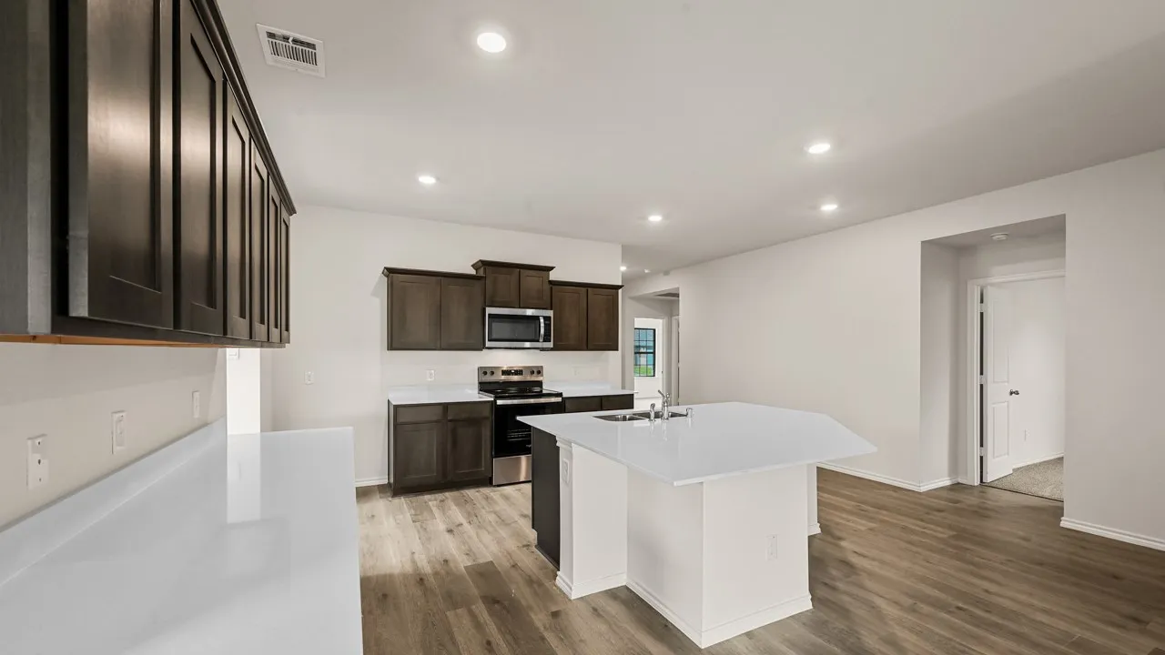 Kitchen featuring dark wood-finish cabinetry, white countertops, built-in stainless steel microwave, and a central island with an integrated sink