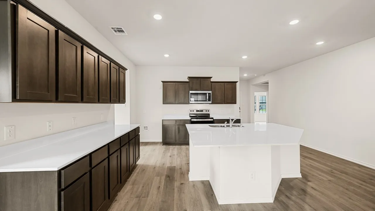 Kitchen featuring wood-finish flooring, dark wood cabinetry, light-toned countertops, a central island with an integrated sink, and recessed lighting