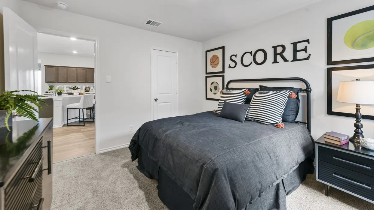 Carpeted bedroom with a solid door, offering a direct line of sight into a kitchen area featuring wood-finish flooring, a breakfast bar, and dark wood cabinetry