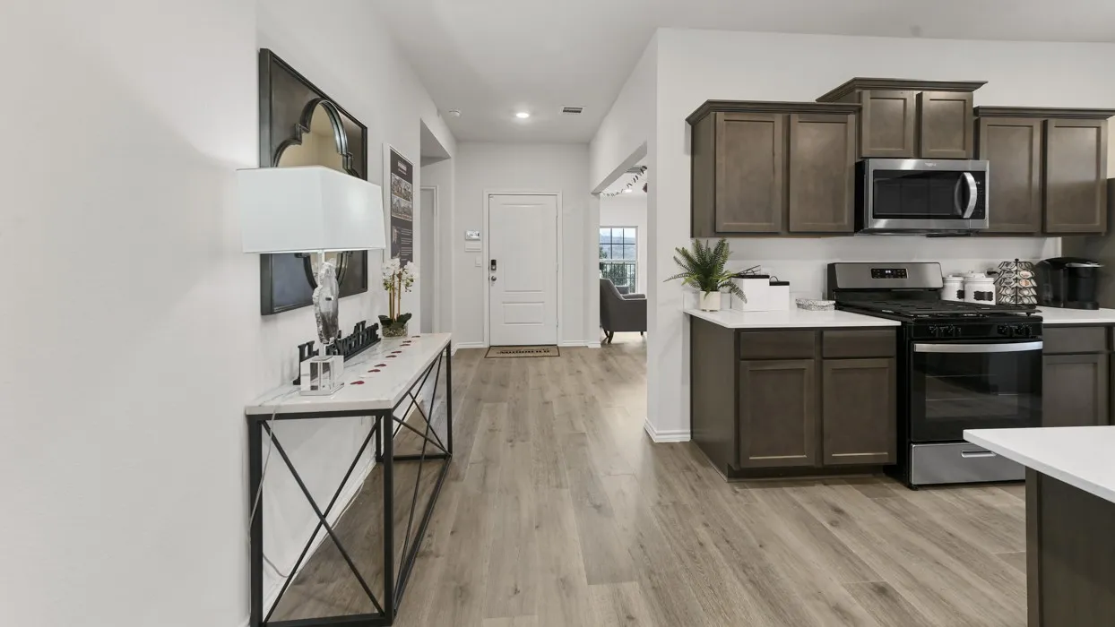 Open-concept living area featuring wood-finish flooring, a kitchen with dark wood cabinetry, stainless steel appliances, and light-colored countertops