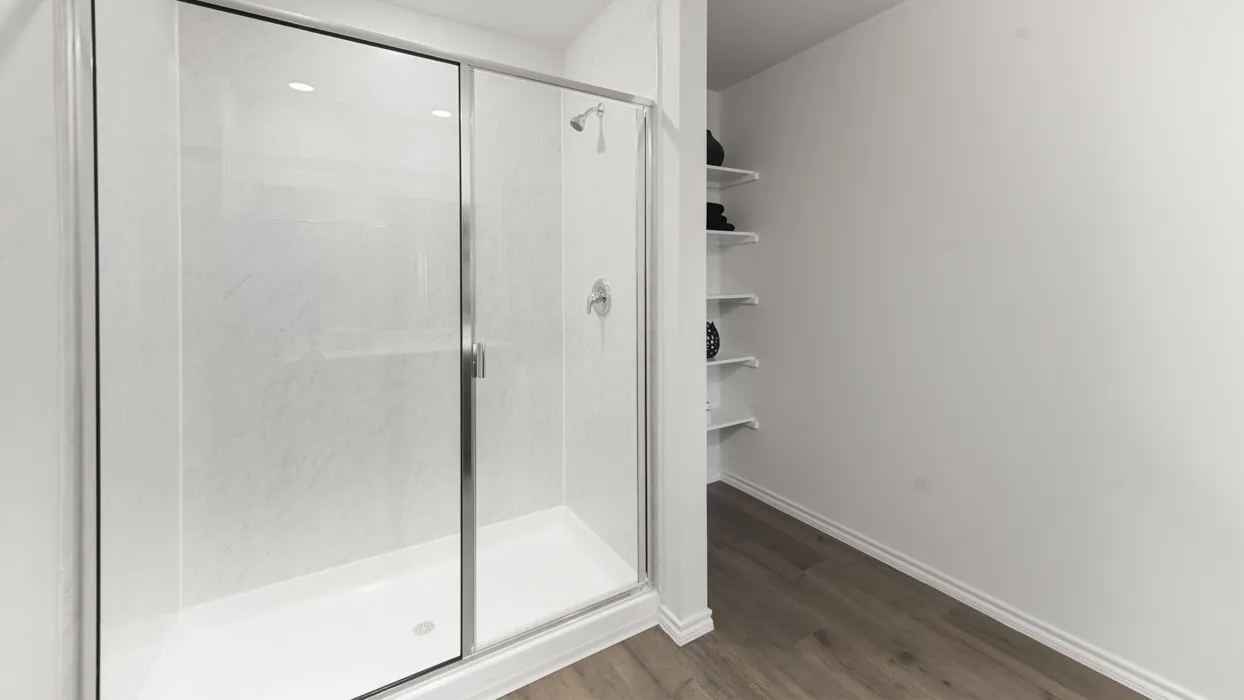 Frameless glass shower enclosure with chrome fixtures and white textured shower walls