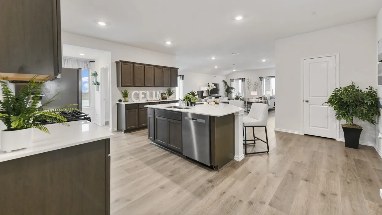 Open-concept kitchen featuring an island with an integrated sink and dishwasher, dark wood-finish cabinetry, light-toned countertops, and wood-finish flooring