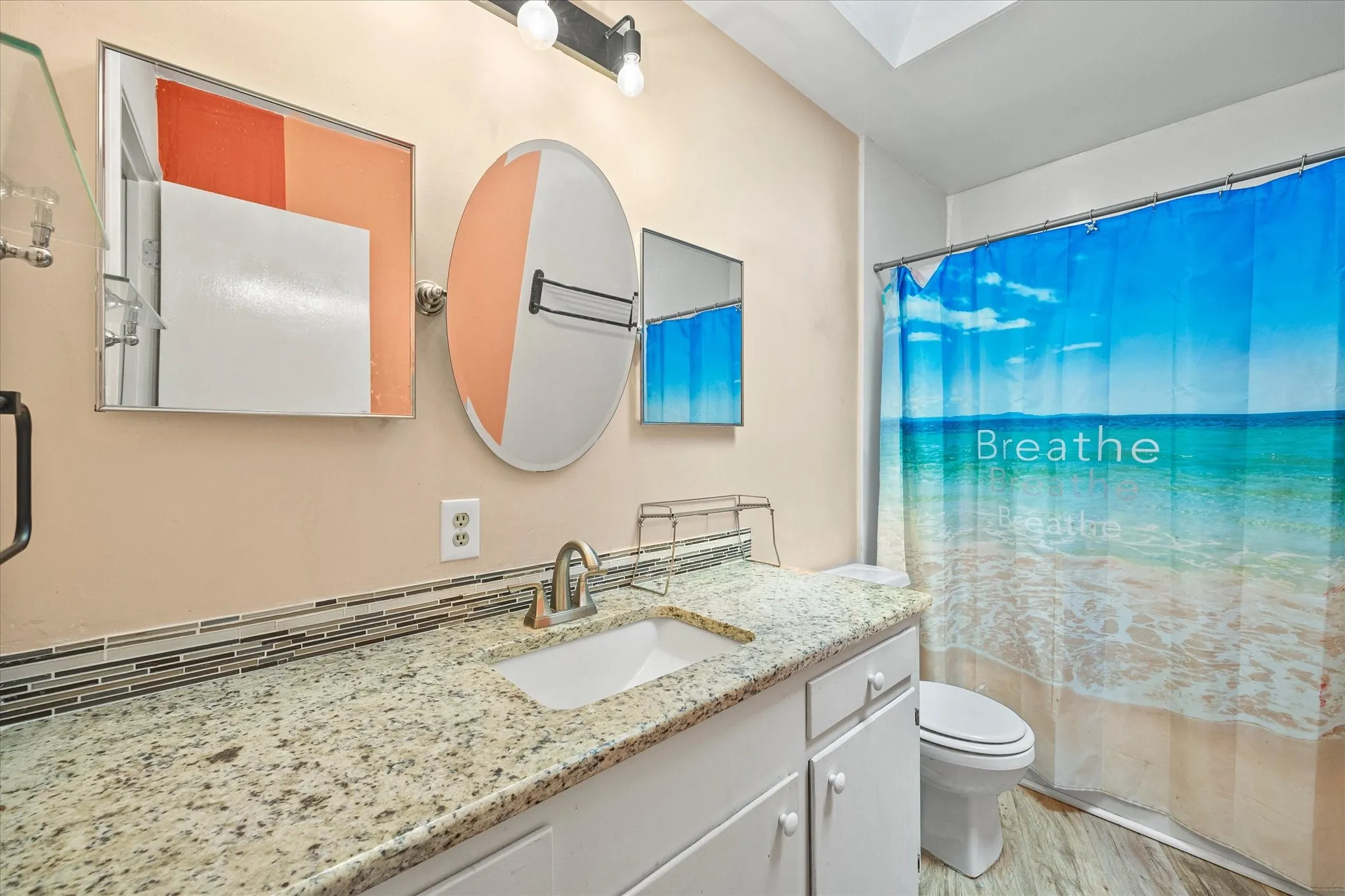 Bathroom featuring a vanity with a light granite-patterned countertop, an undermount sink, a chrome-finish faucet, white cabinetry, and a tile backsplash