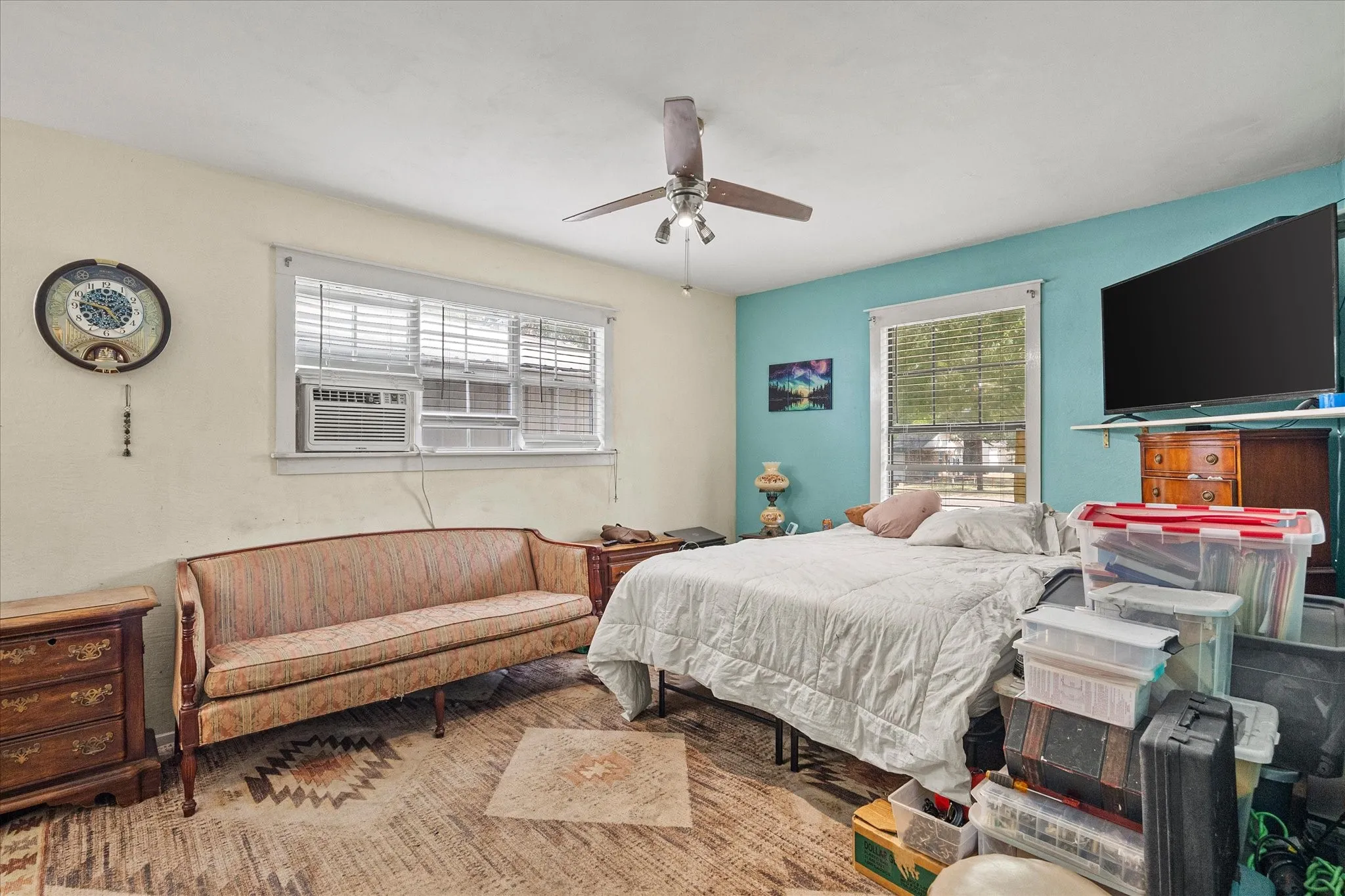 Ceiling fan fixture, window with blinds, window air conditioning unit, light-colored walls, and wood-finish flooring