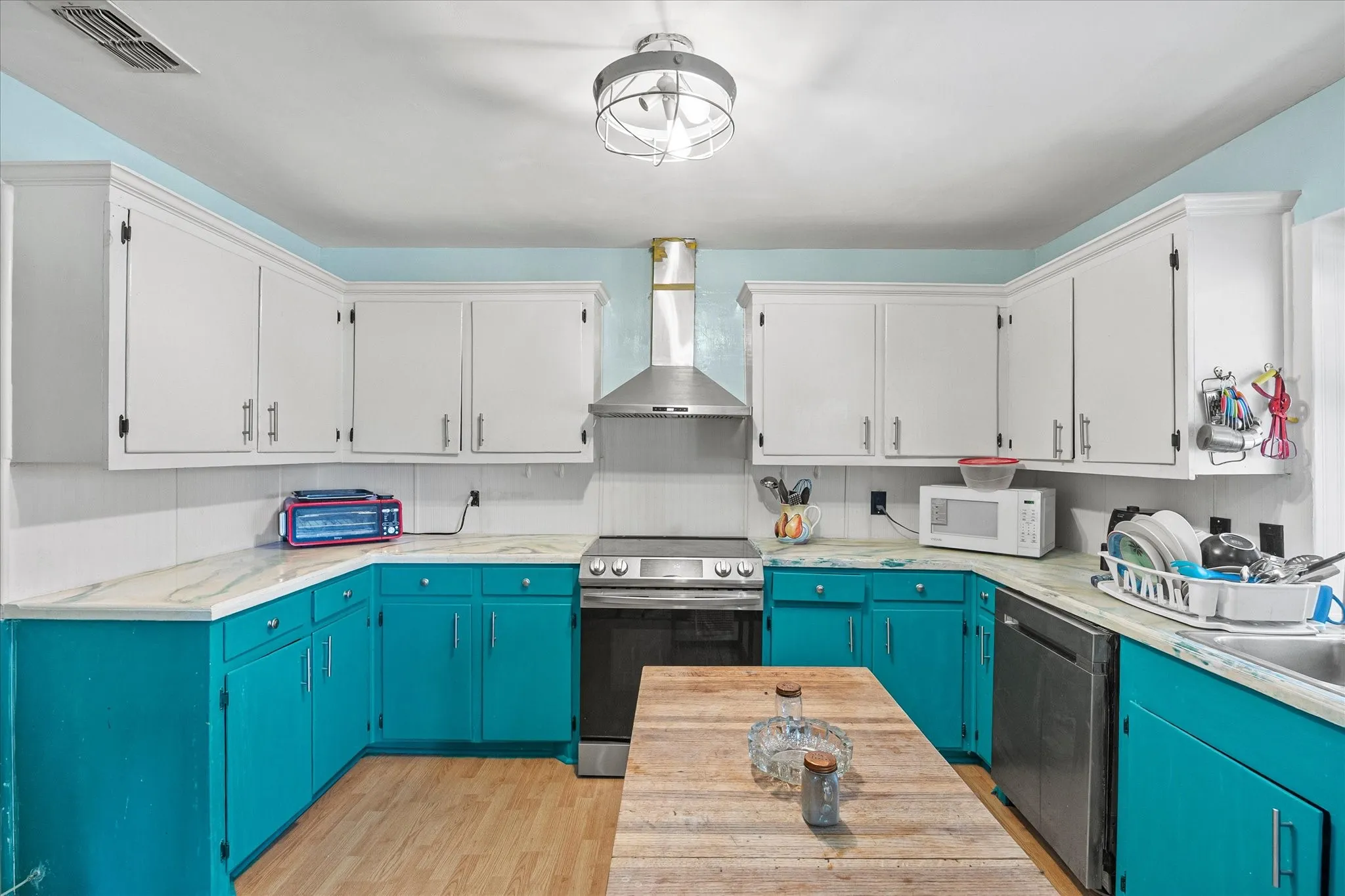 U-shaped kitchen featuring white upper cabinetry, teal lower cabinetry, light-toned countertops, and wood-finish flooring