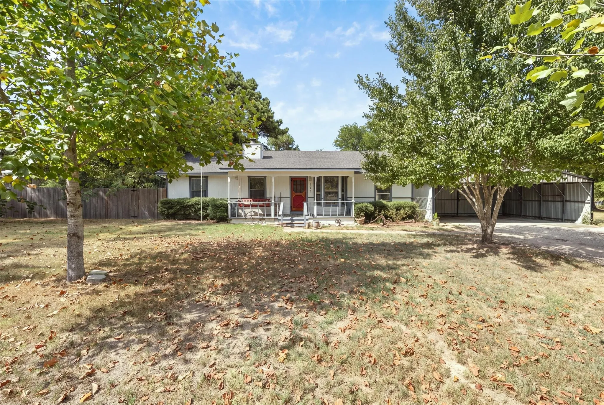 Single-story residence featuring a covered front porch, a red entry door, a covered carport, and a wood privacy fence