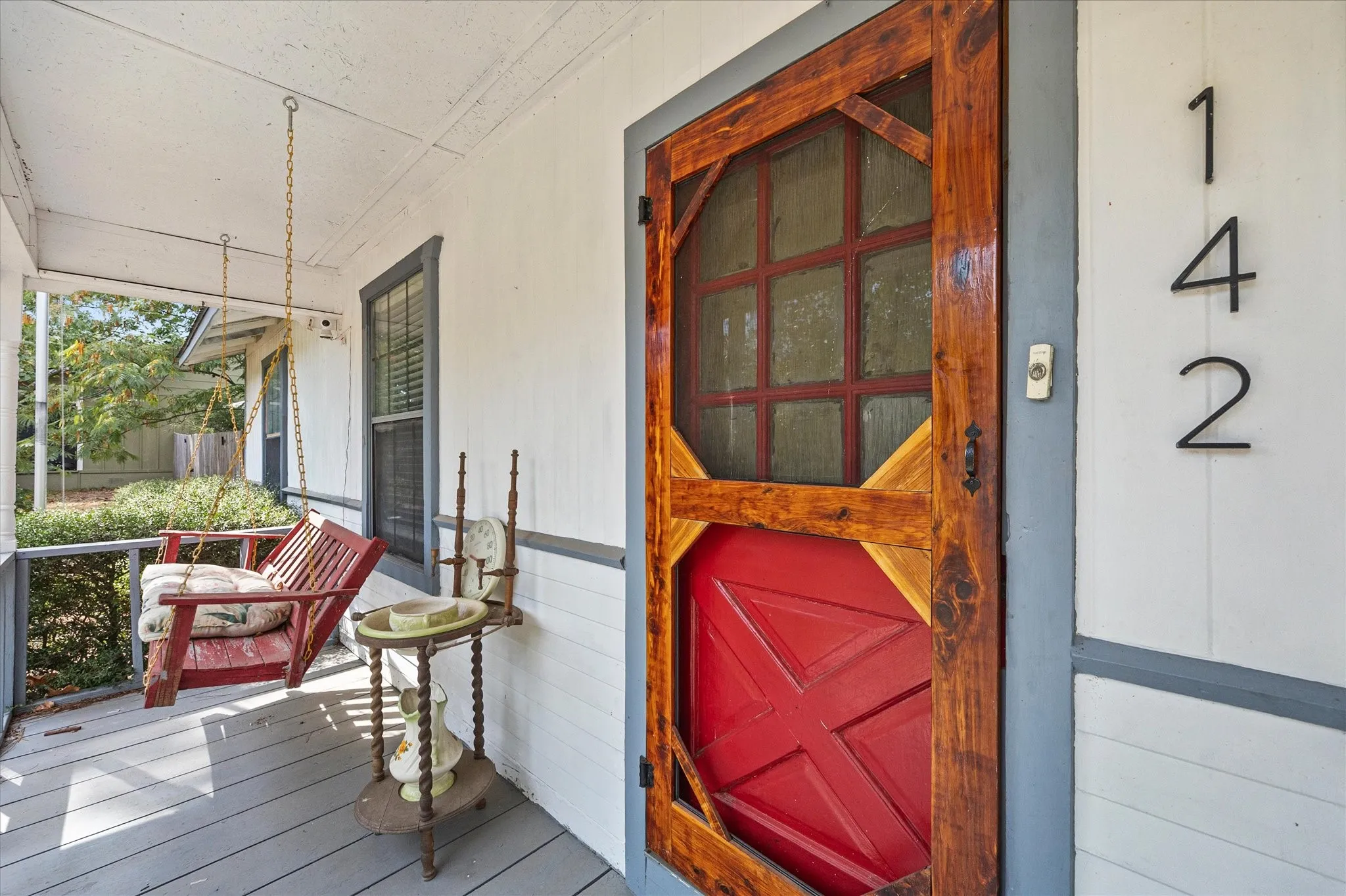 Covered front porch with a wood-finish swing and a vibrant red front door
