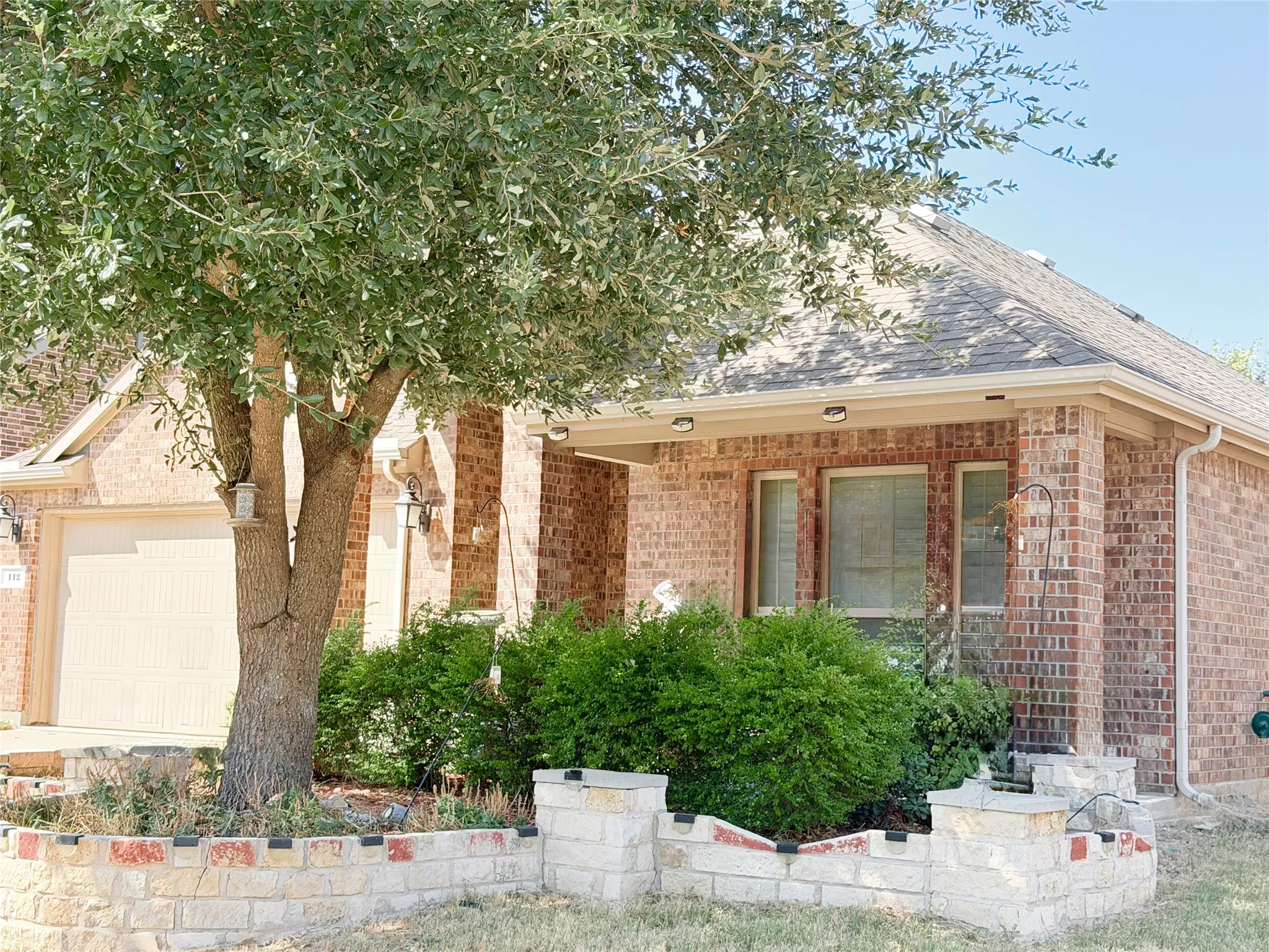 Brick exterior with a covered entry, composition shingle roof, and an attached garage