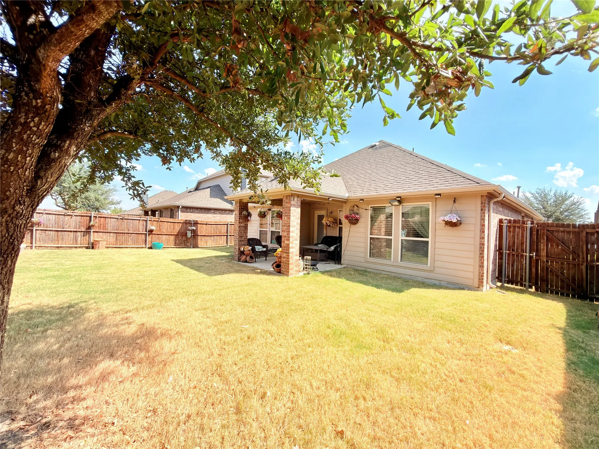 Expansive grass lawn with mature trees, a covered patio featuring brick columns, and a wood privacy fence