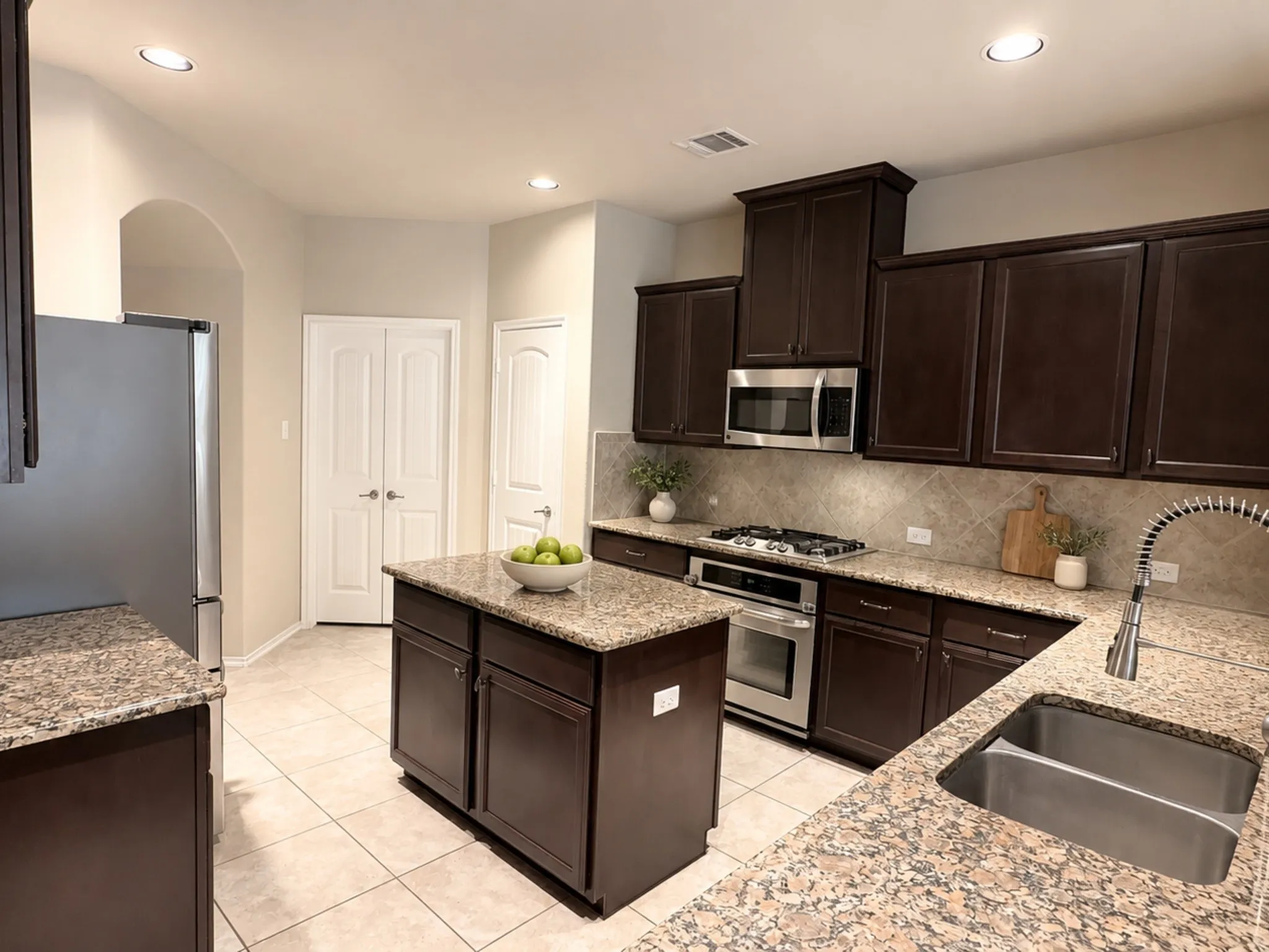 Kitchen featuring a central island, dark wood-finish cabinetry, light-toned tile flooring, and stainless steel appliances