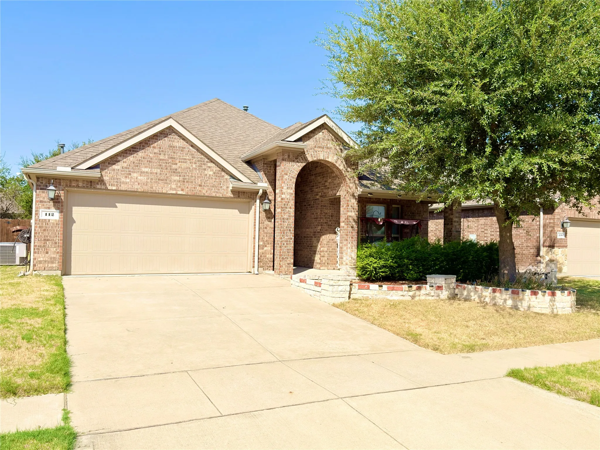 Brick exterior with an arched entry, attached garage, and a concrete driveway