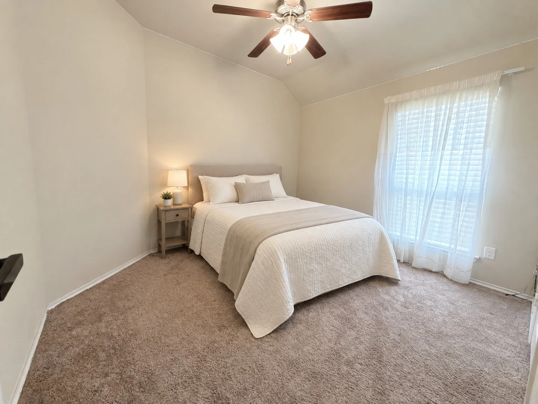 Vaulted ceiling, ceiling fan with integrated lighting, window with blinds, and neutral tone carpeting. VIRTULY STAGED