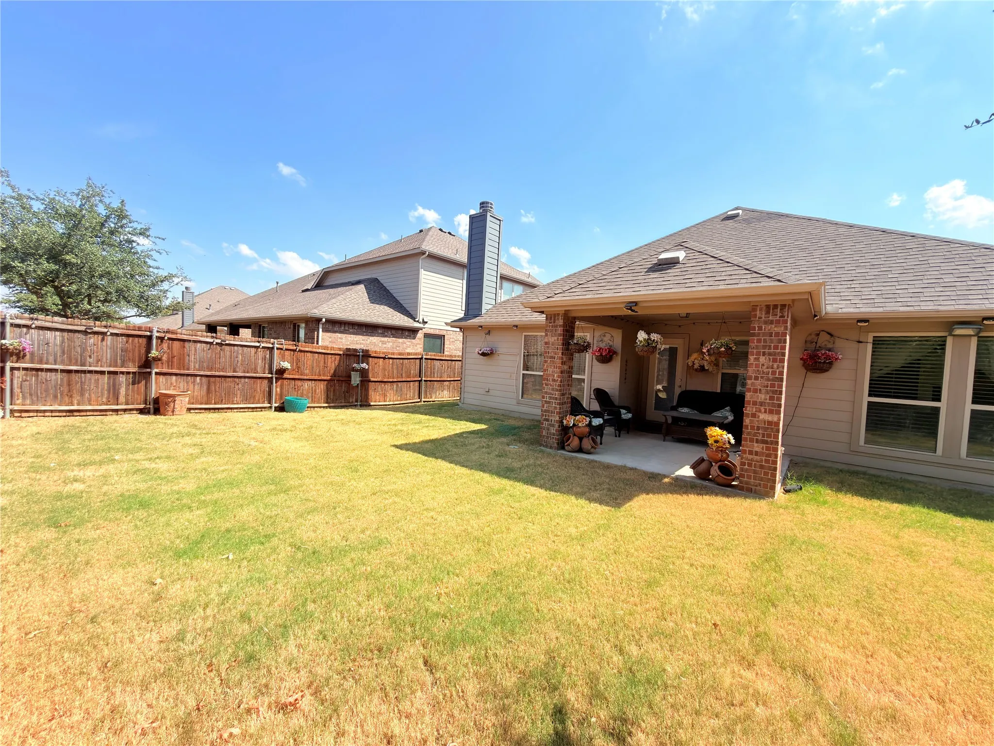 Expansive backyard with a wooden fence, covered patio featuring brick columns, and a shingle roof
