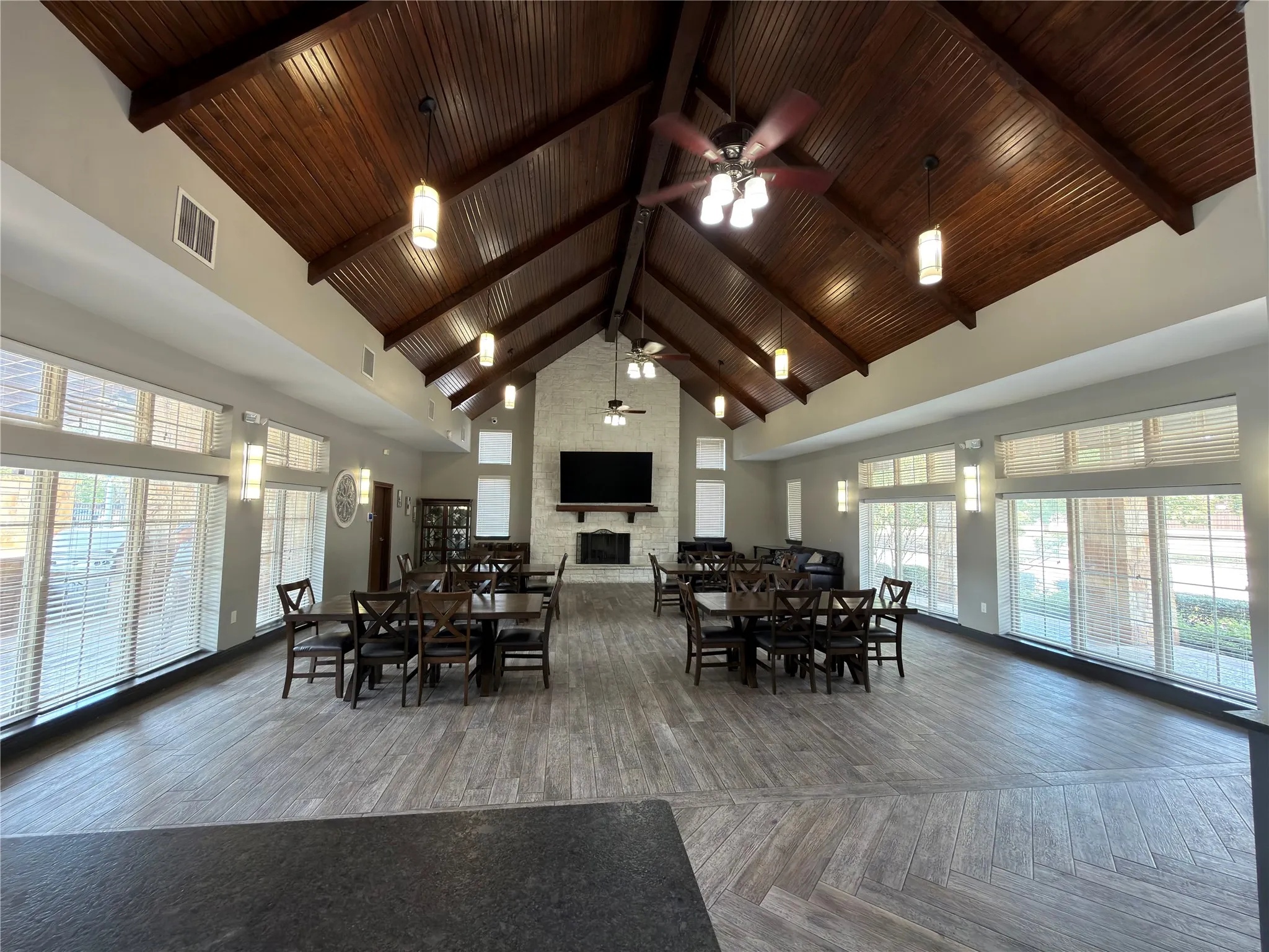 Vaulted wood-finish ceilings, wood-finish flooring with herringbone pattern, stone-finish fireplace, and multiple windows with horizontal blinds