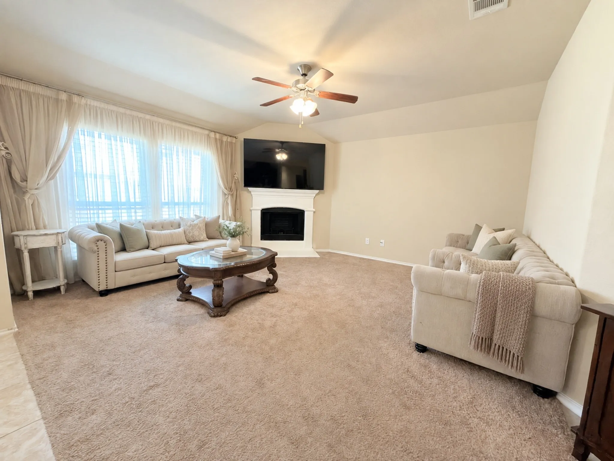 Wall-to-wall carpeting, vaulted ceiling with a ceiling fan, large window with natural light, and a built-in fireplace with mantel