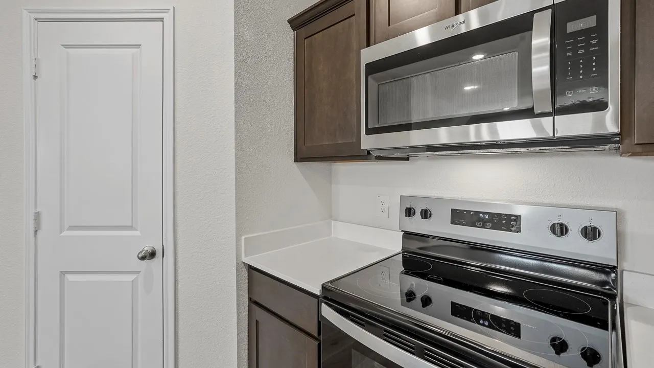 Stainless steel microwave, stainless steel electric range, dark wood-finish cabinetry, light-toned countertop, and white panel door