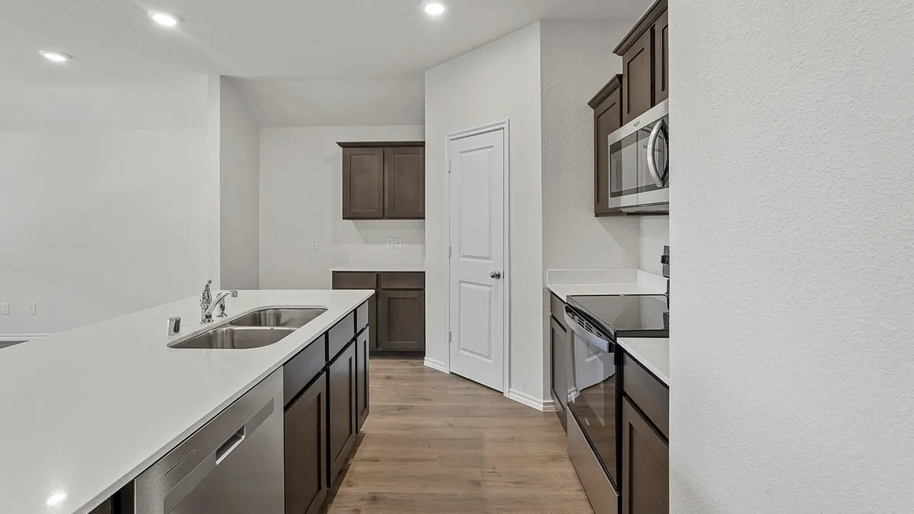 Kitchen featuring an island with double stainless steel sinks, white countertops, dark wood cabinetry, and stainless steel appliances
