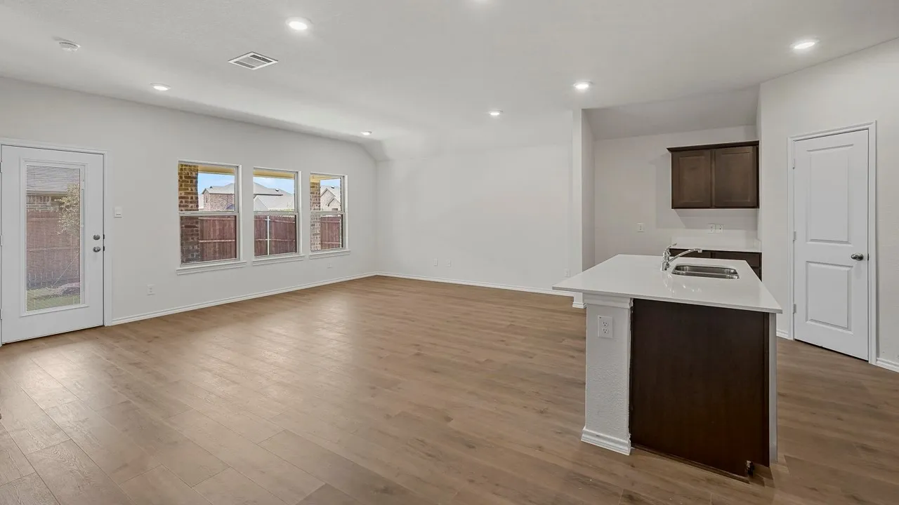Wood-finish flooring, recessed lighting, multiple windows, a kitchen island with a stainless steel sink, and white countertops