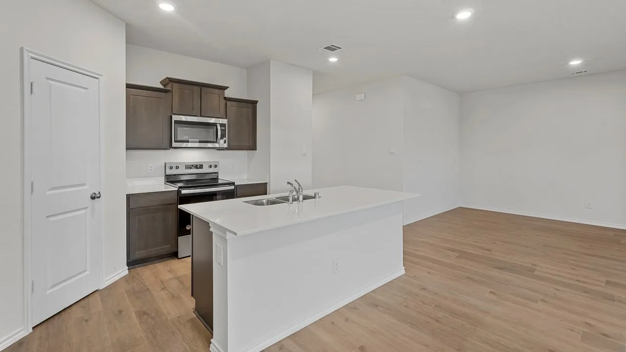 Open-concept kitchen featuring dark wood cabinetry, stainless steel appliances, a white tile backsplash, and an island with a built-in sink