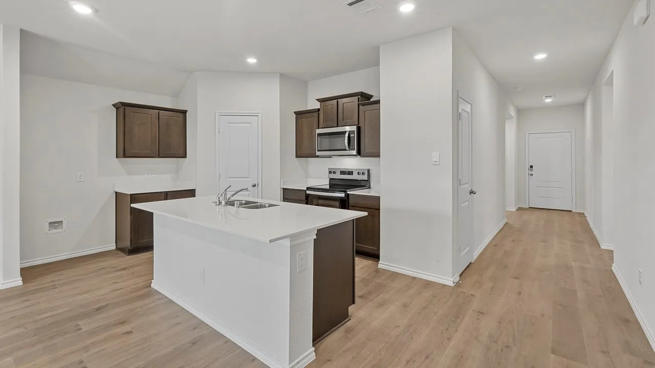 Kitchen featuring an island with an integrated sink, dark wood cabinetry, white countertops, and stainless steel appliances