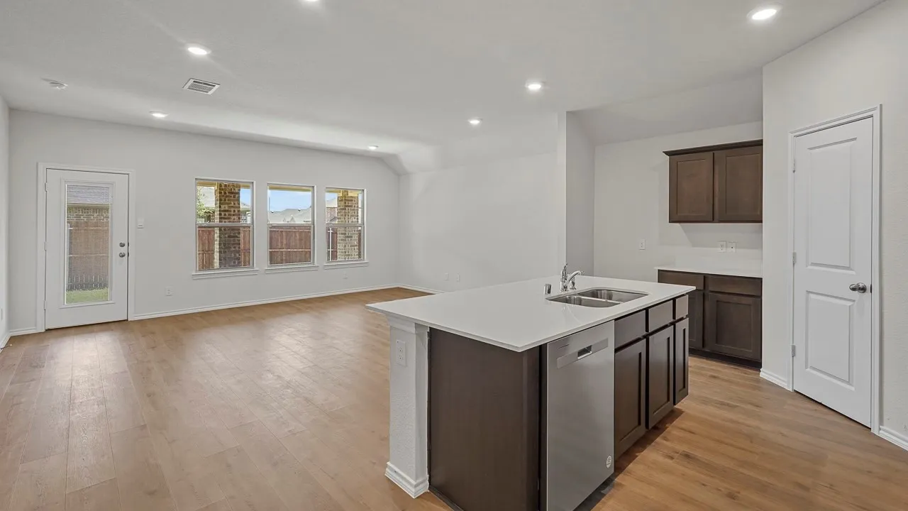 Open-concept interior featuring wood-finish flooring, recessed lighting, and a kitchen island with an integrated stainless steel sink