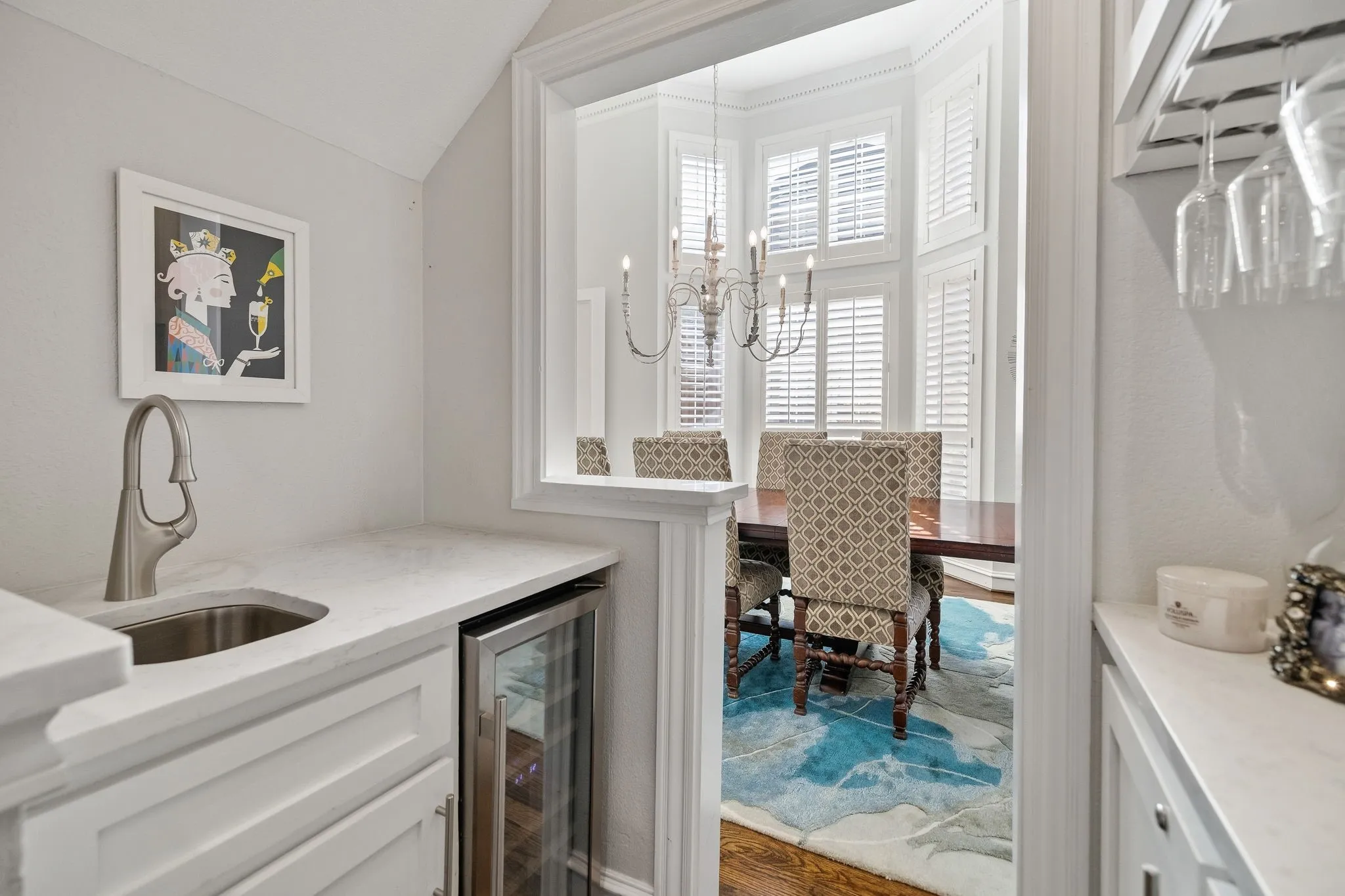 Renovated wet bar with custom cabinetry, wine storage, wine glass display, sink & wine fridge.