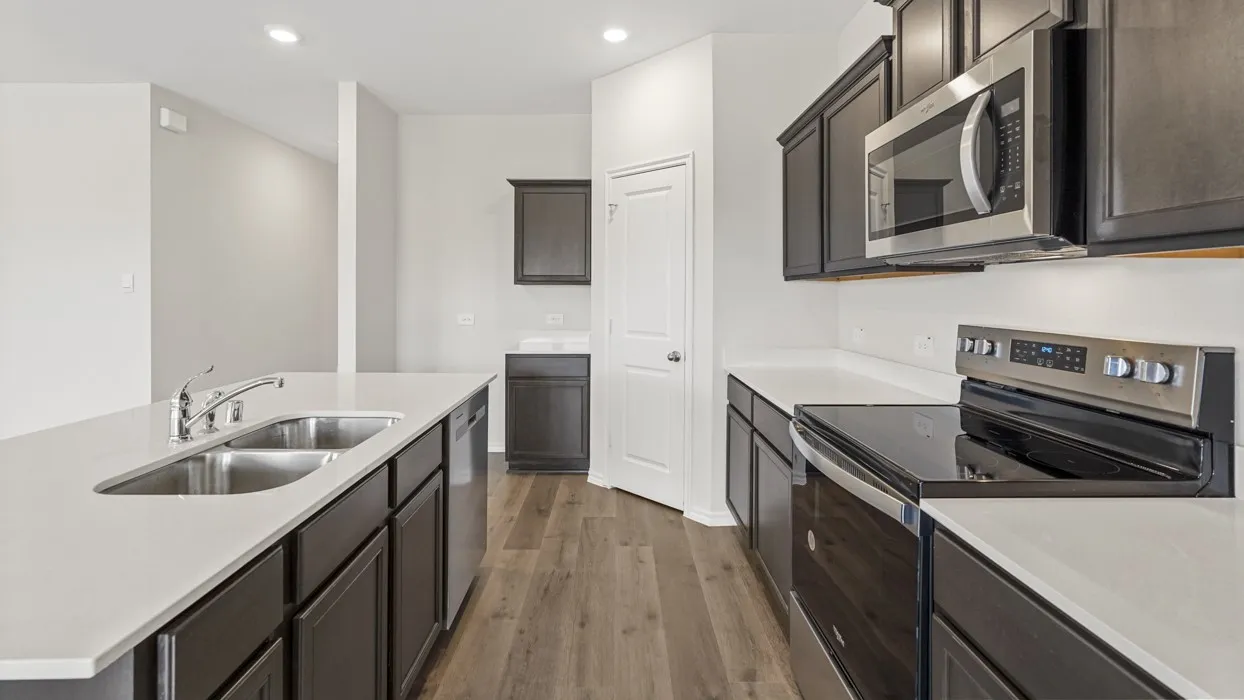 Modern kitchen featuring stainless steel appliances, dark wood cabinetry, light countertops, a double basin sink, and wood-finish flooring